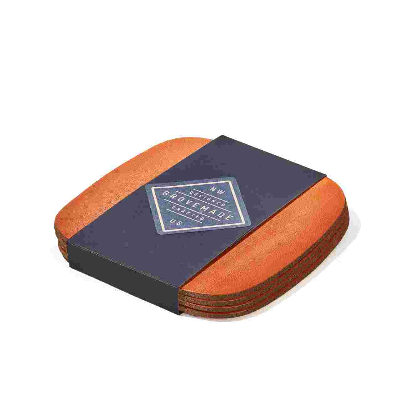 Set of four tan leather coasters in black paper packaging.