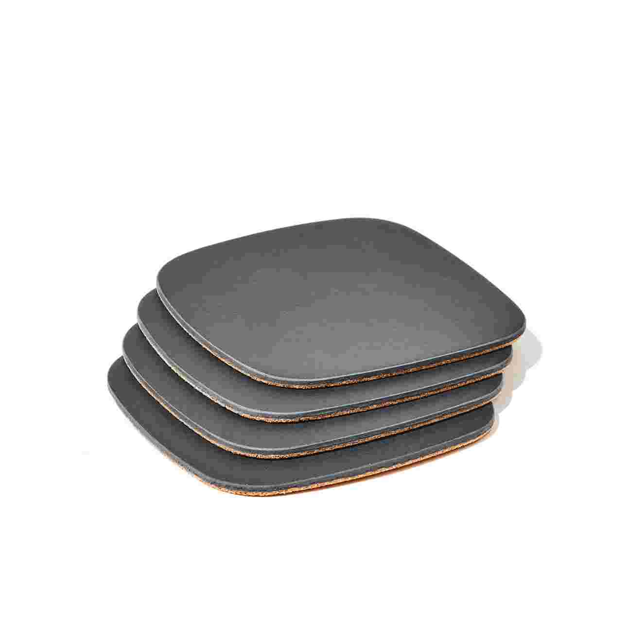 Stack of four matte black coasters with cork padding.
