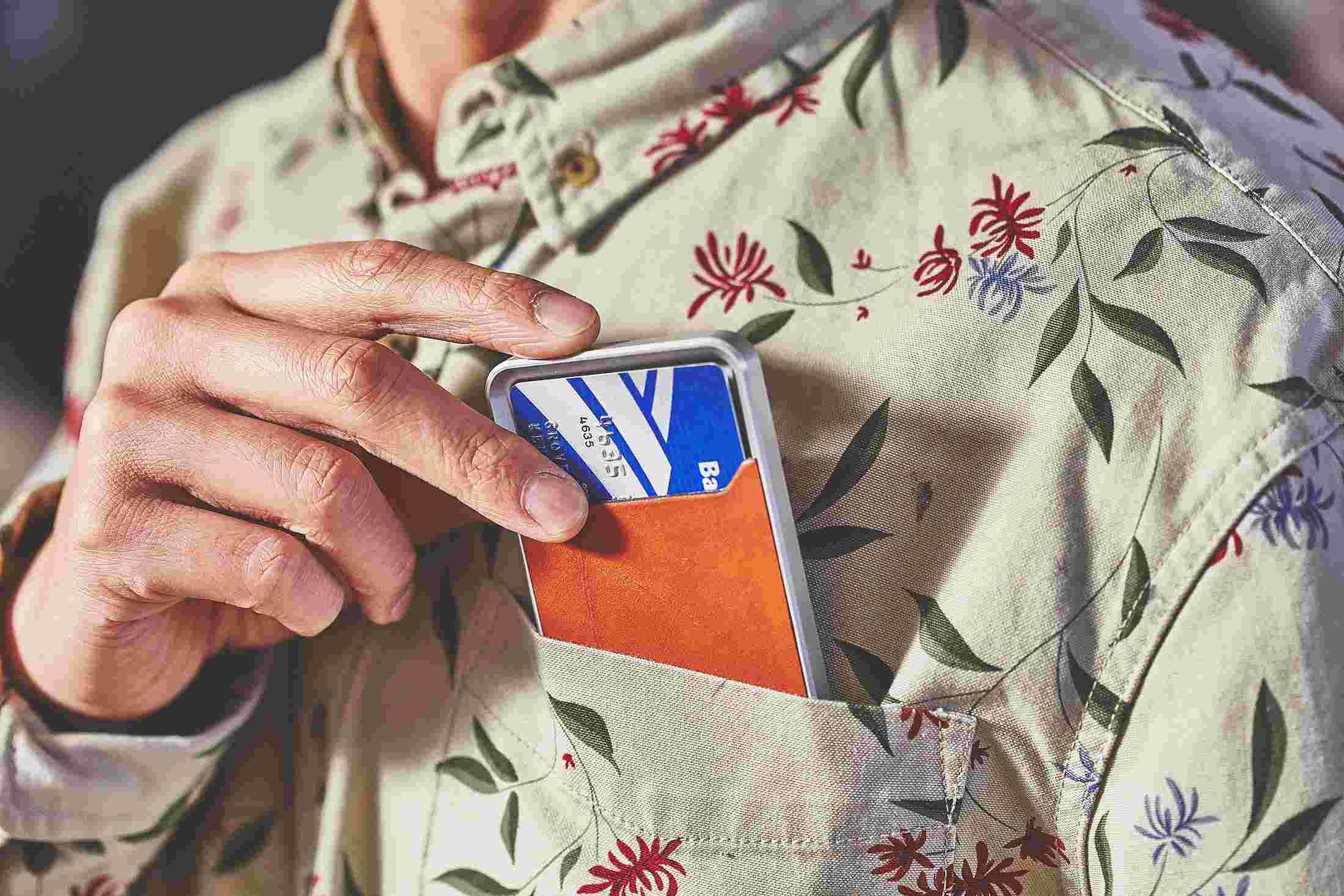 Hand inserting tan minimalist wallet into shirt pocket.