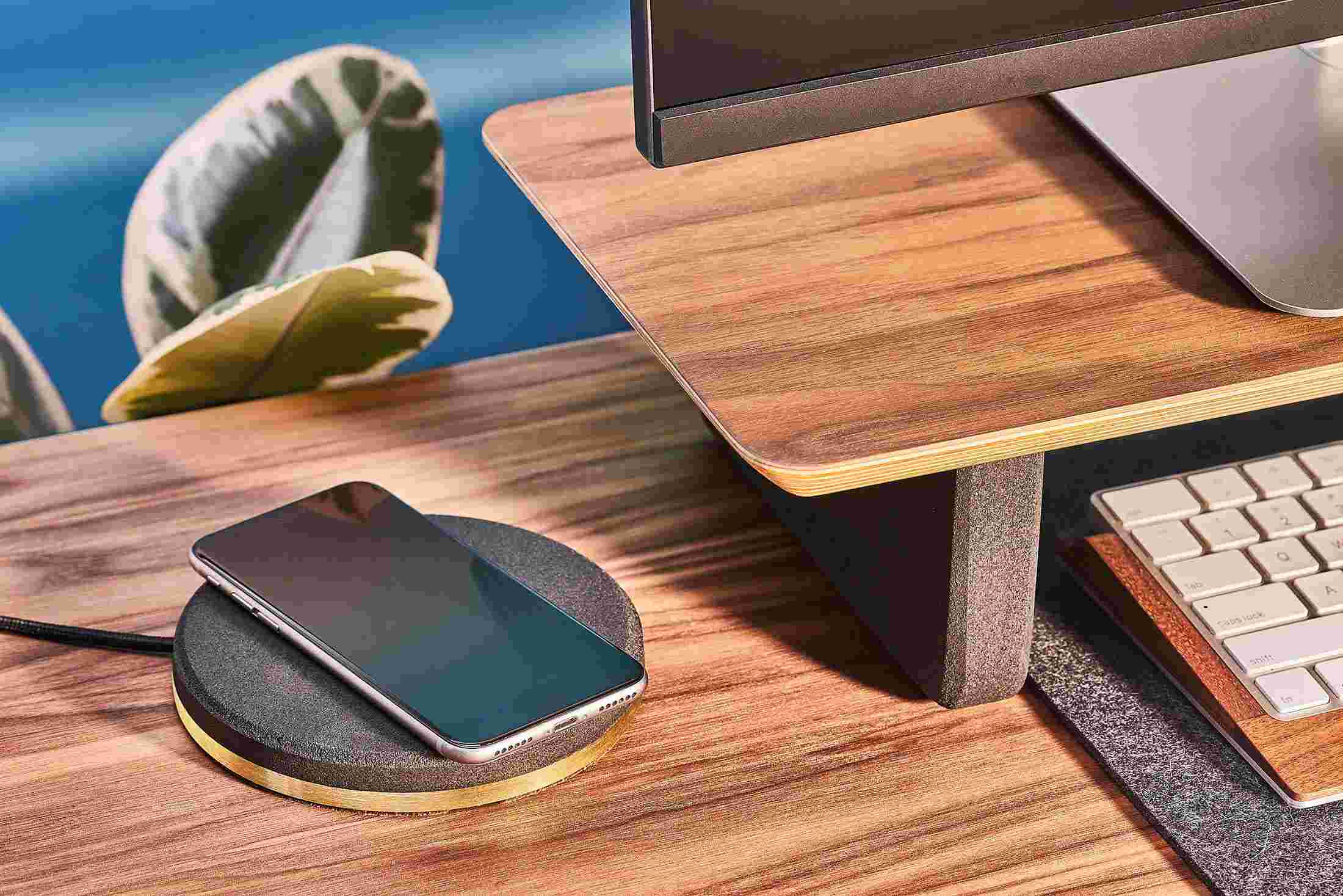 The Brass iPhone Charging Pad topped with black cork, matching the black cork leg of the desk shelf.