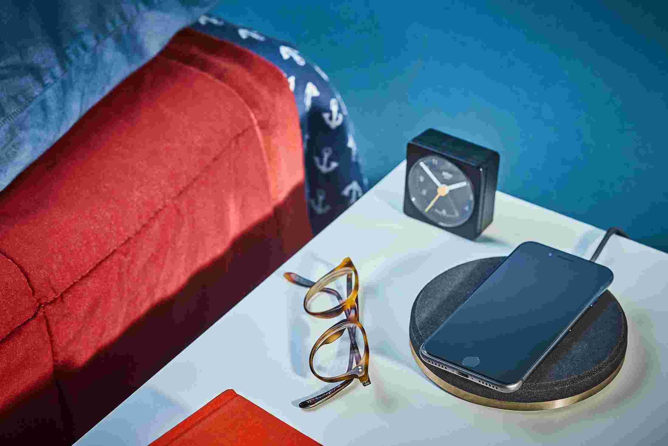 Black and brass wireless charging pad on bedside table charging an iPhone X.