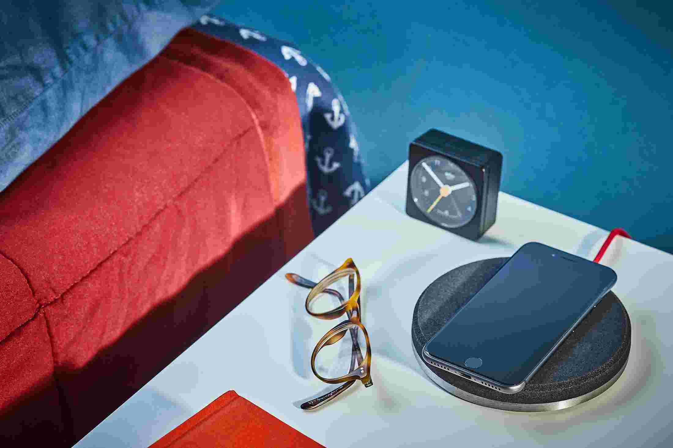 Black wireless charging pad on bedside table charging an iPhone X.
