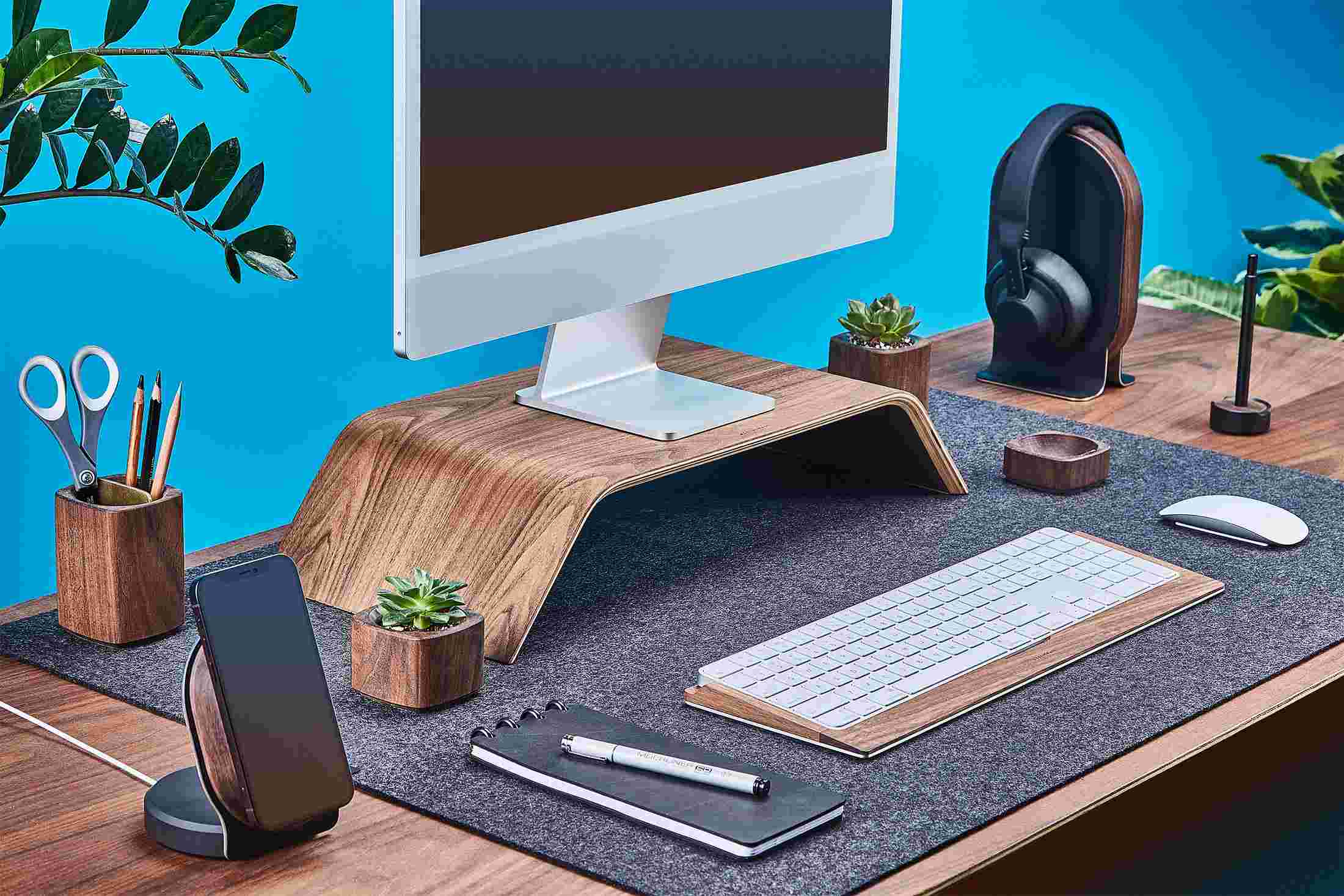 Side view of the walnut wood Grovemade Desk Collection with walnut wood monitor stand, pen cup, planters, keyboard tray and headphone stand.