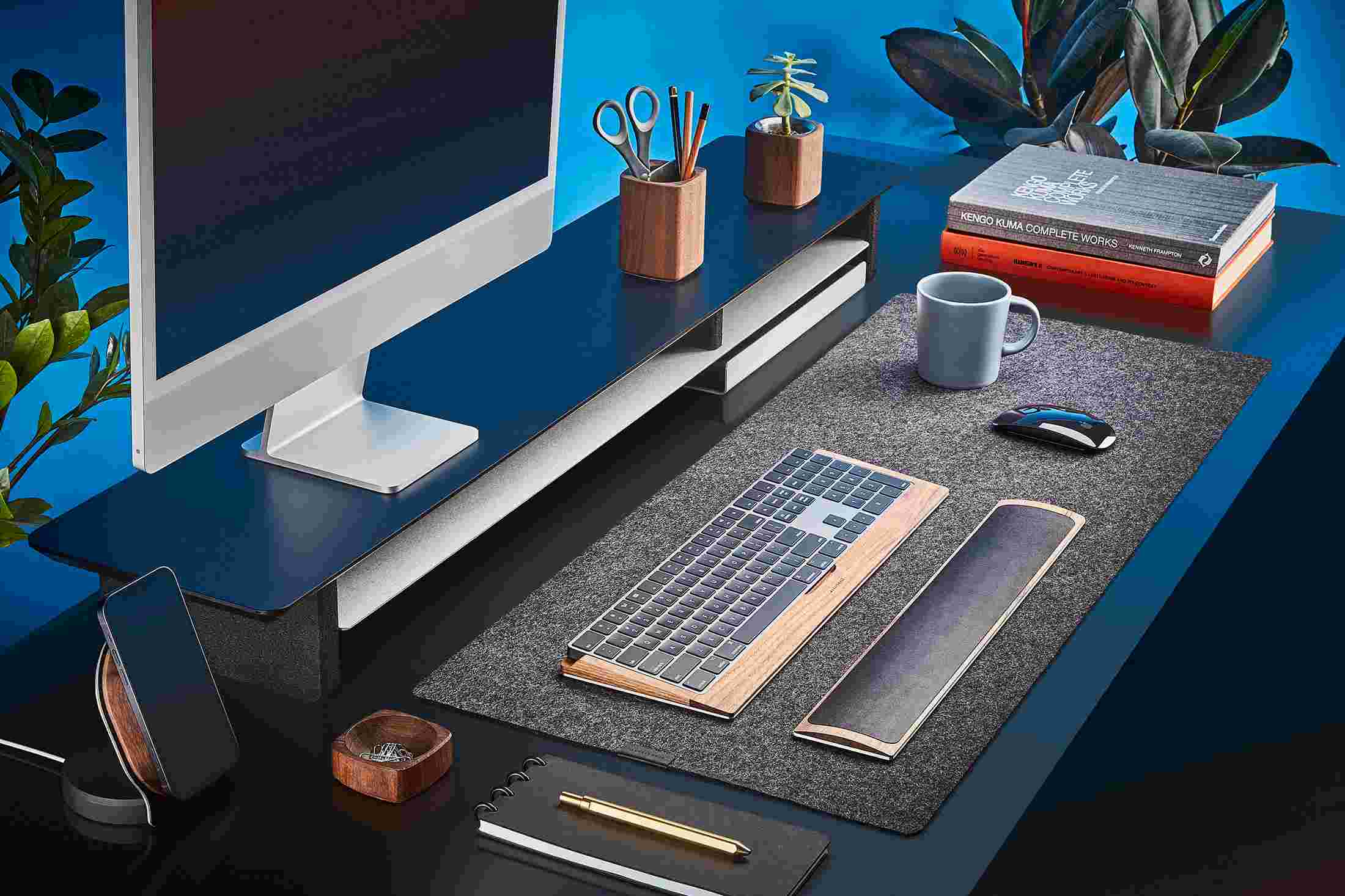 The Medium Plus Wool Felt Desk Pad runs the entire width of a standard desk, pictured here with matte black double-wide monitor stand.