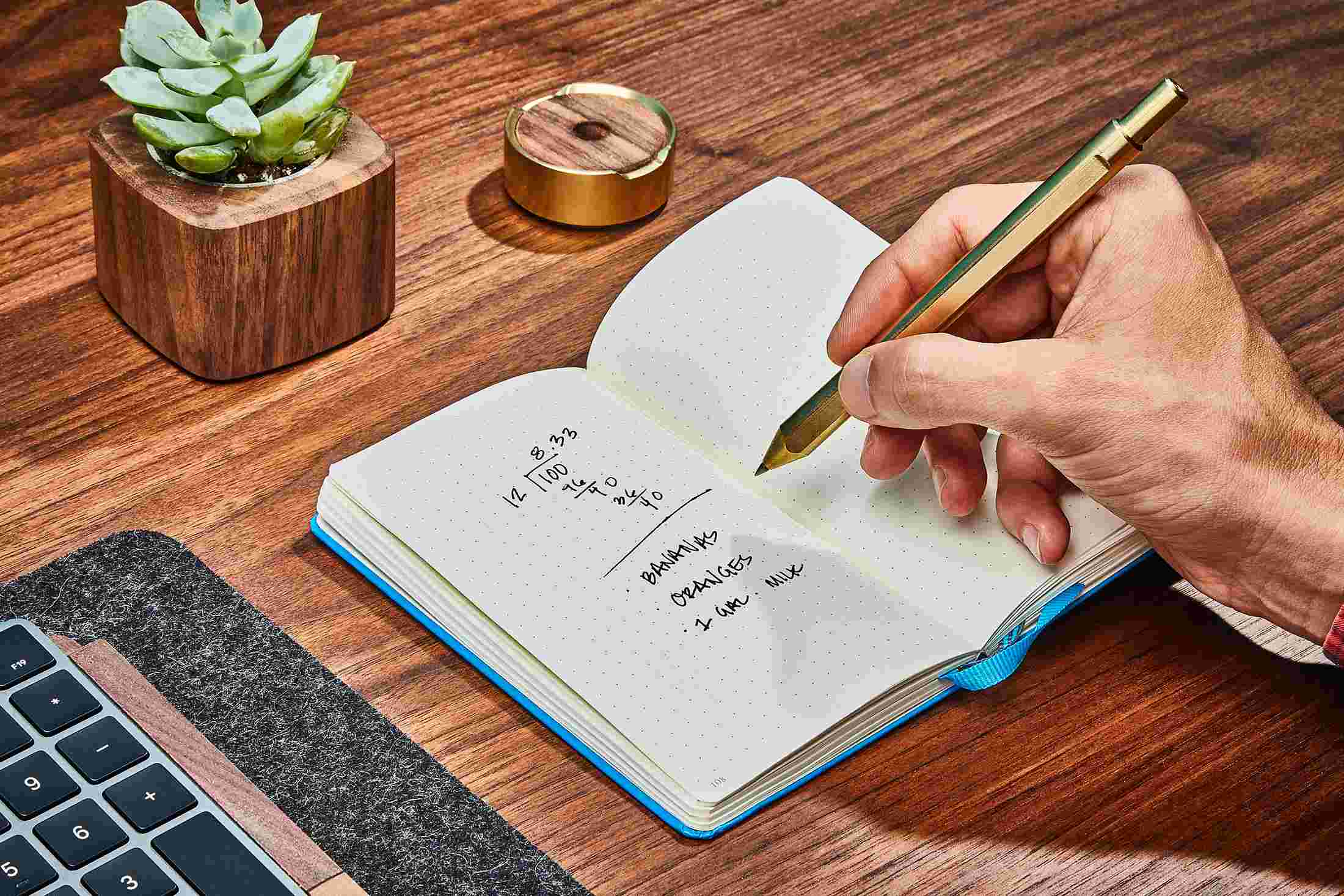 The Grovemade Brass Pen in use, writing in a notebook.