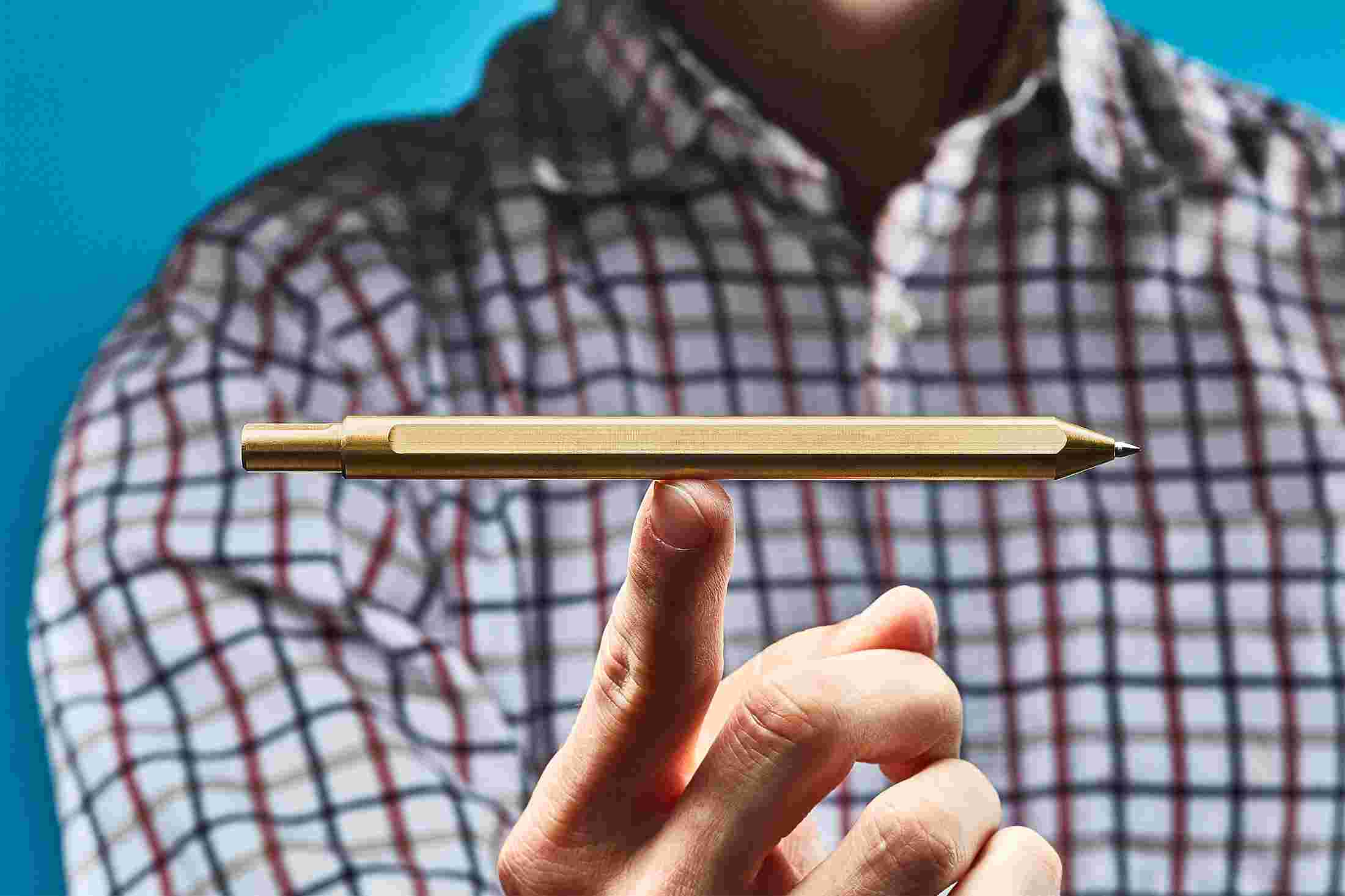 The brass pen perched on a single finger, showing the extreme balance of the minimalist design.