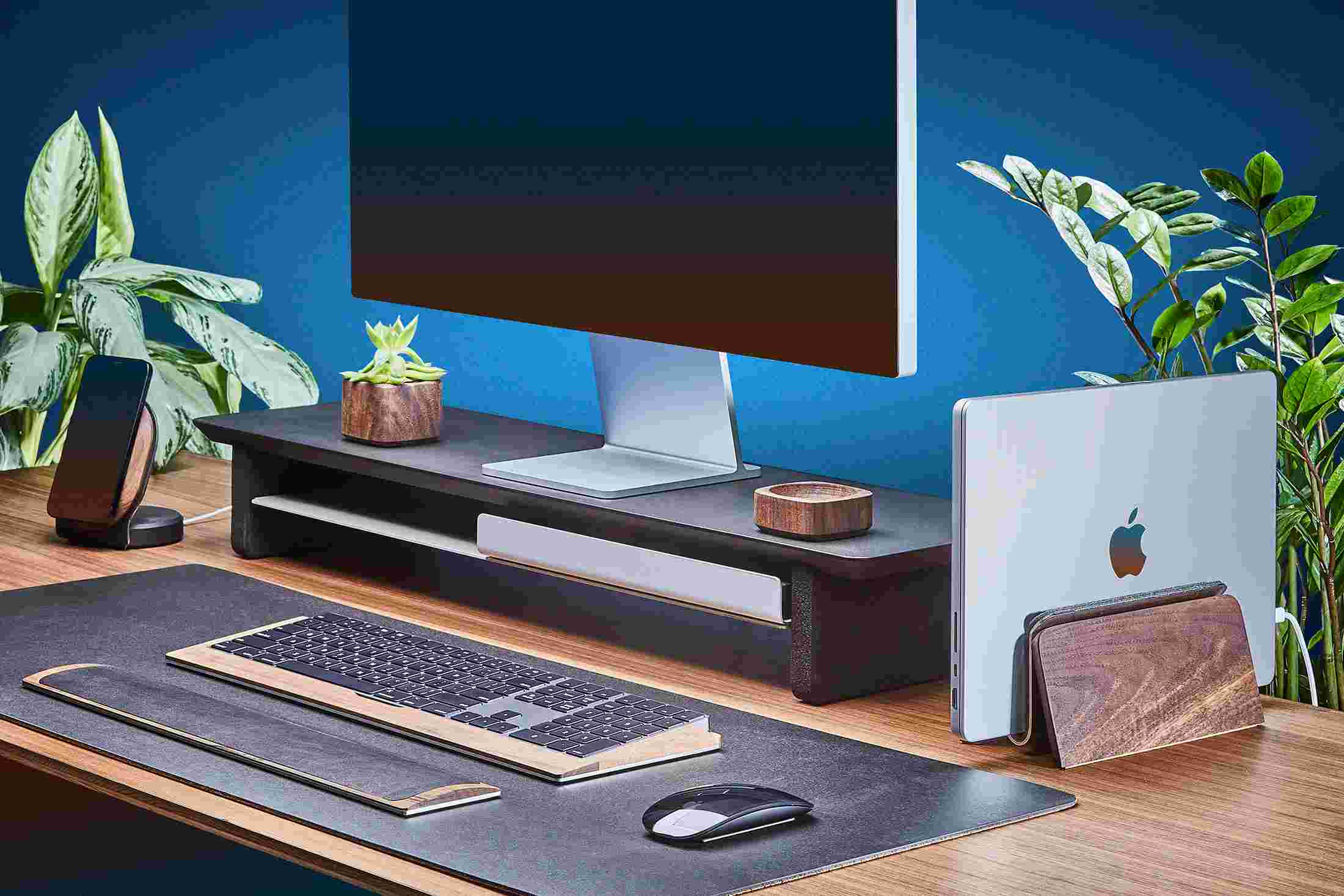 Space saving vertical MacBook Dock and medium matte black monitor stand, with black leather desk pad.