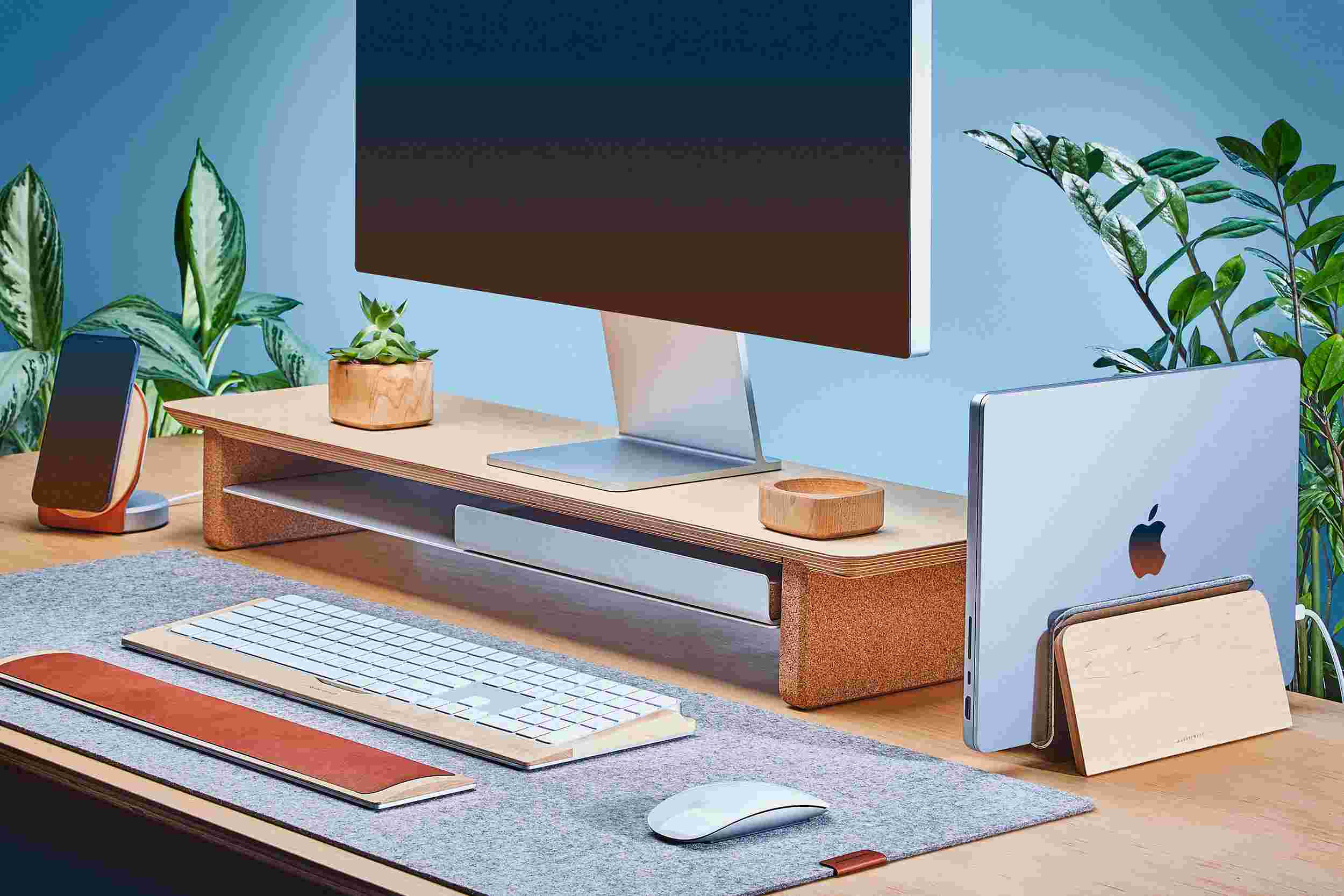 Space saving vertical MacBook Dock and medium wooden maple monitor stand, with light grey felt desk pad.
