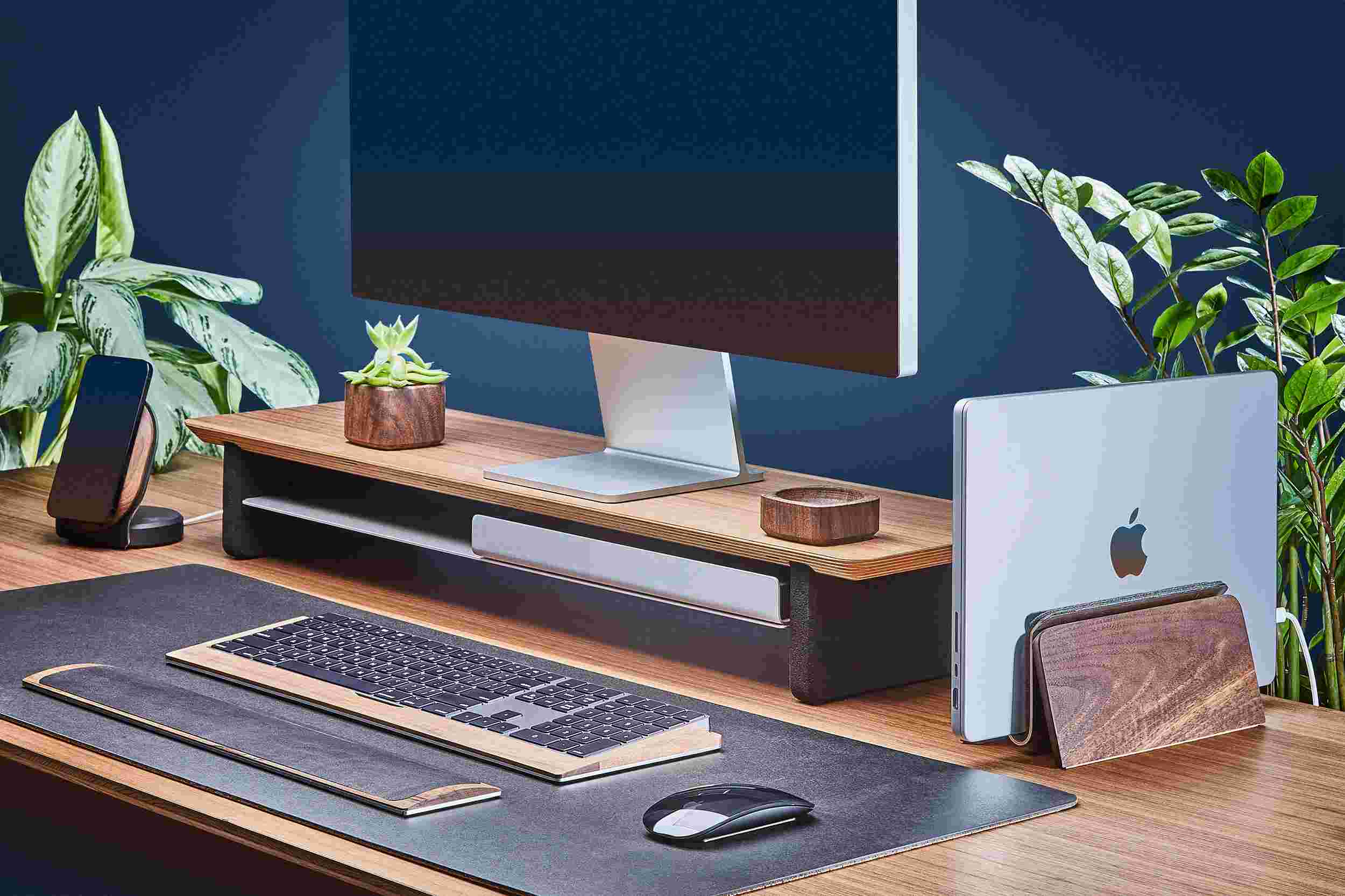 Space saving vertical MacBook Dock and medium wooden walnut monitor stand, with black leather desk pad.