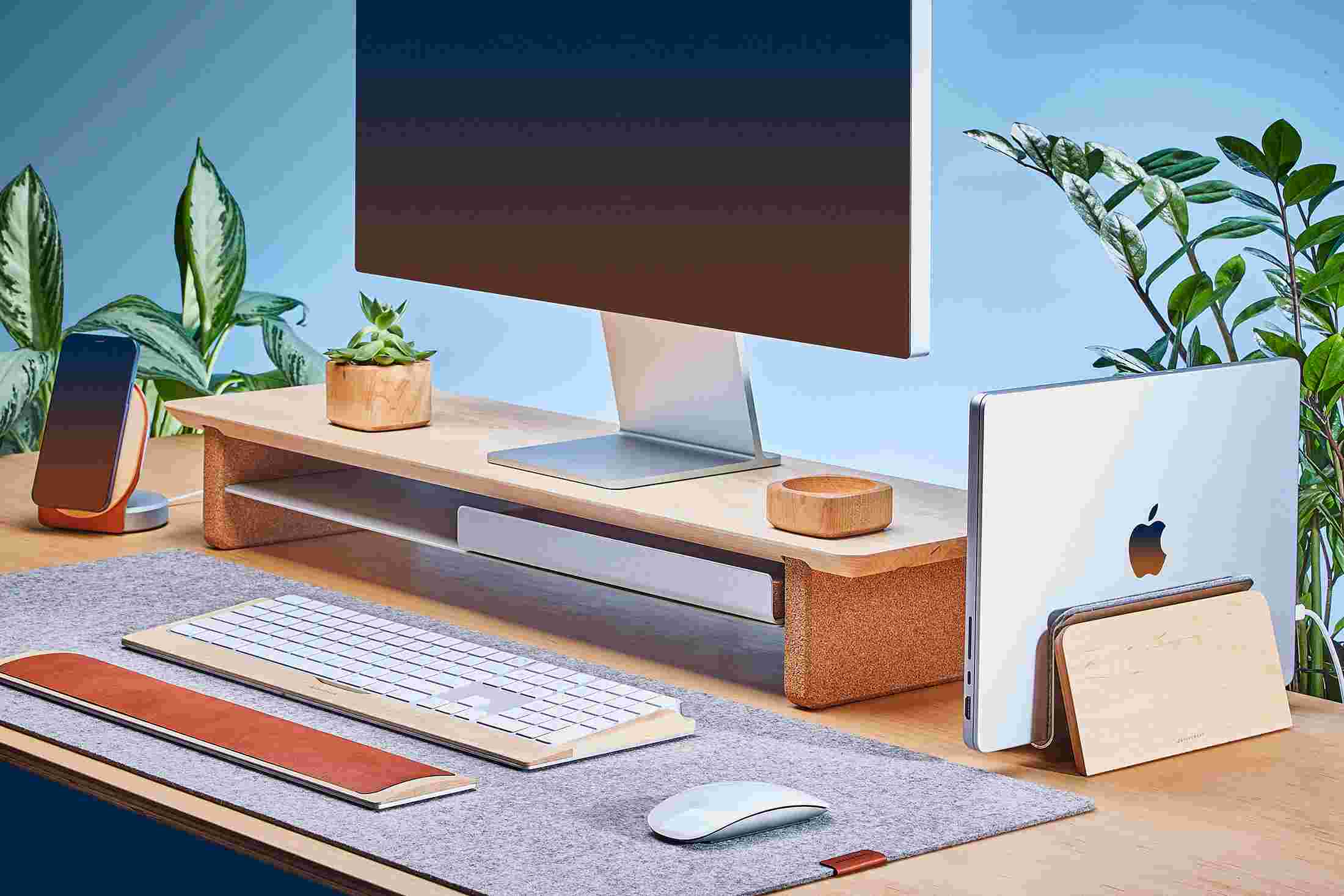Space saving vertical MacBook Dock and medium hardwood maple monitor stand, with light grey felt desk pad.