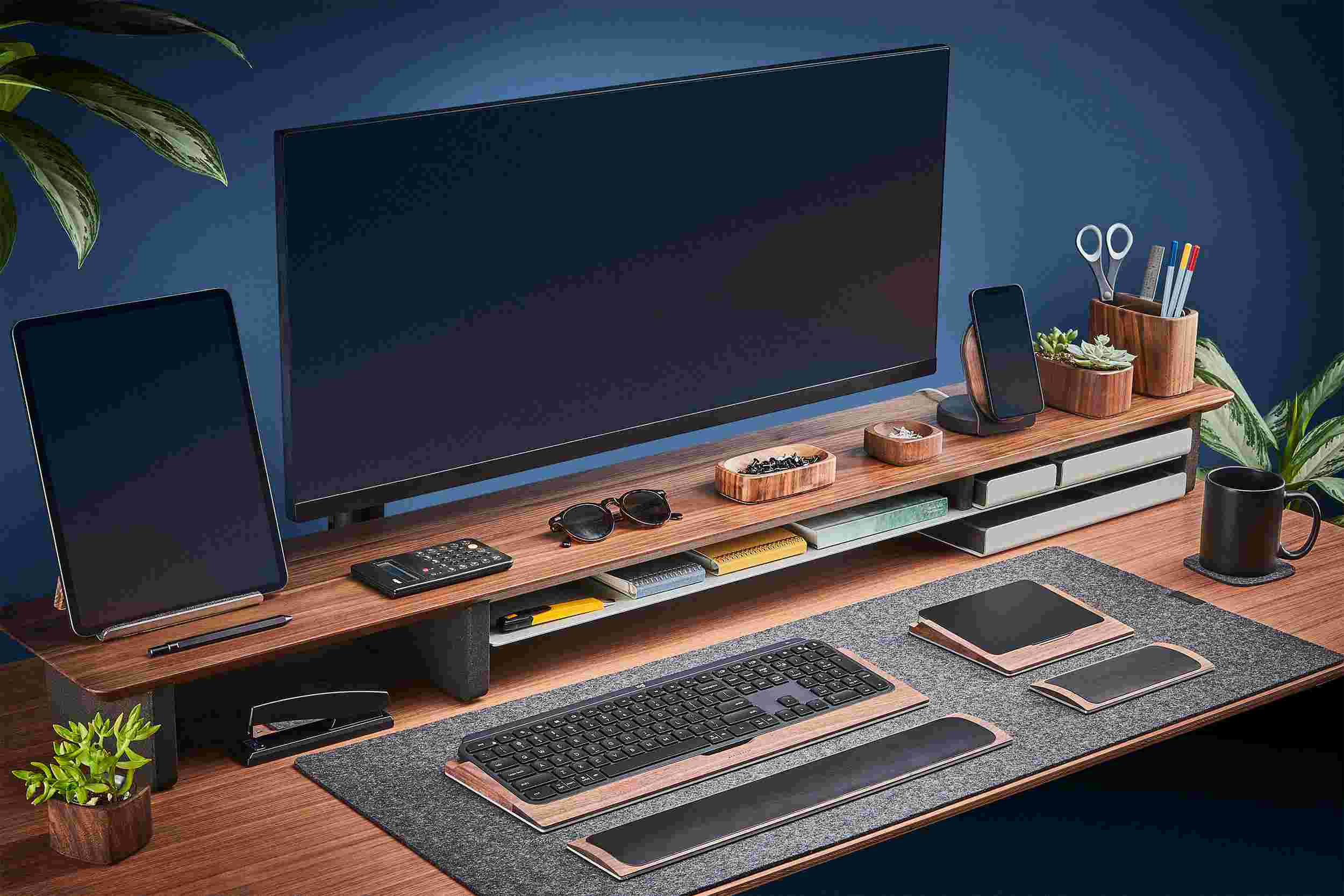 The Medium Wool Felt Desk Pad runs the entire width of a standard desk, pictured here with solid walnut wood double-wide monitor stand.