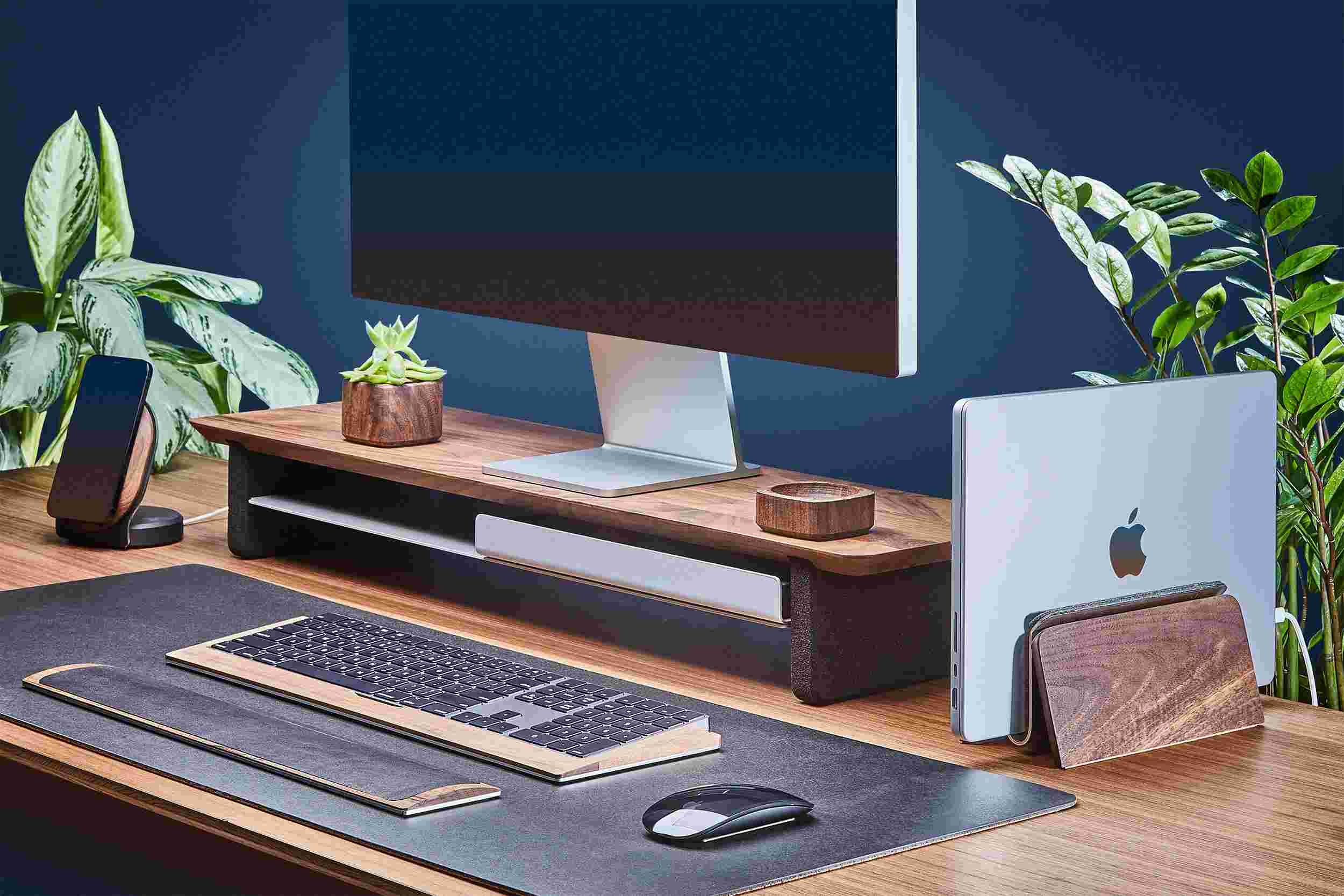 Space saving vertical MacBook Dock and medium hardwood walnut monitor stand, with black leather desk pad.