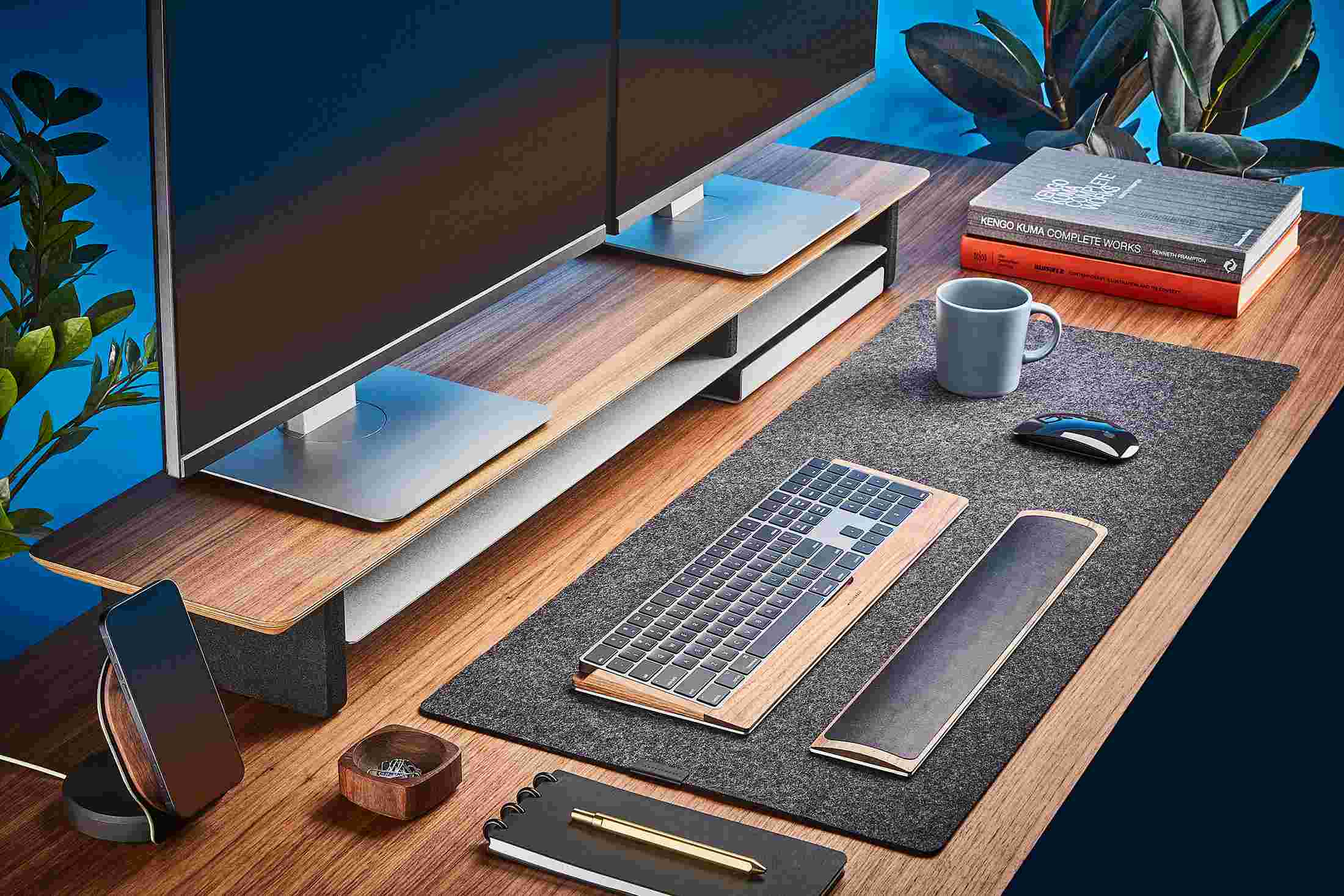 The Medium Plus Wool Felt Desk Pad runs the entire width of a standard desk, pictured here with walnut wood double-wide monitor stand.