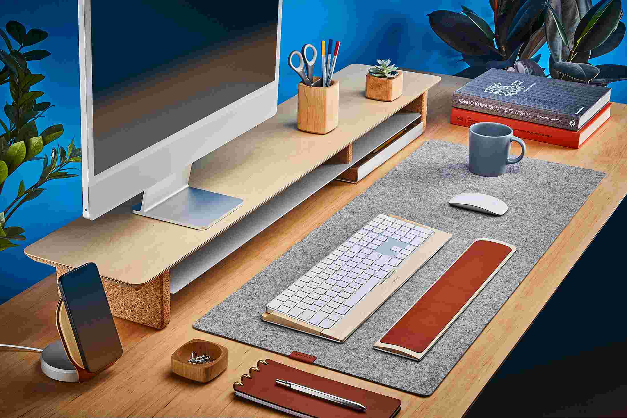 The Medium Plus Wool Felt Desk Pad runs the entire width of a standard desk, pictured here with maple wood double-wide monitor stand.