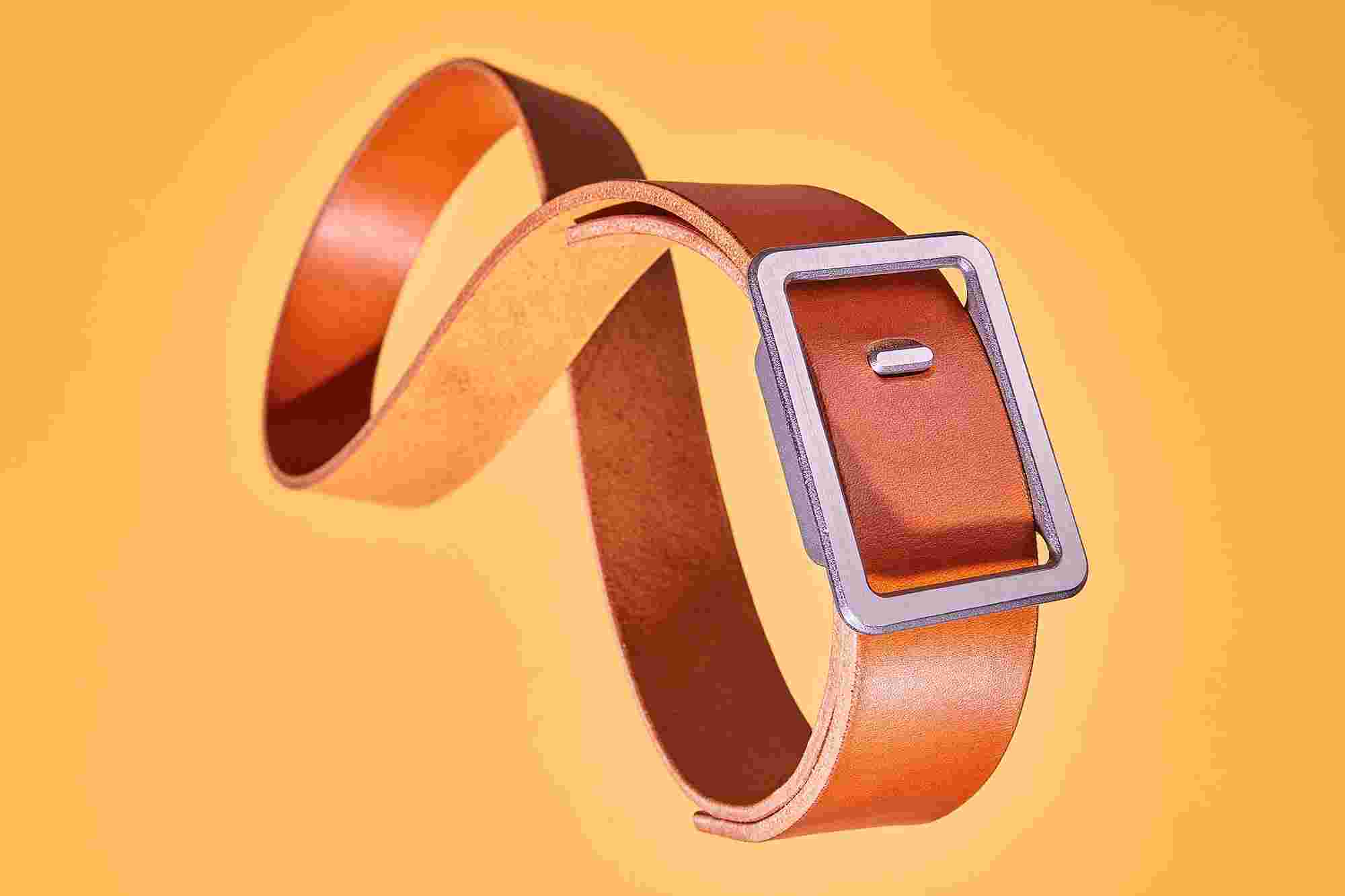Tan minimalist belt in a figure-eight shape, levitating in air on a yellow backdrop.