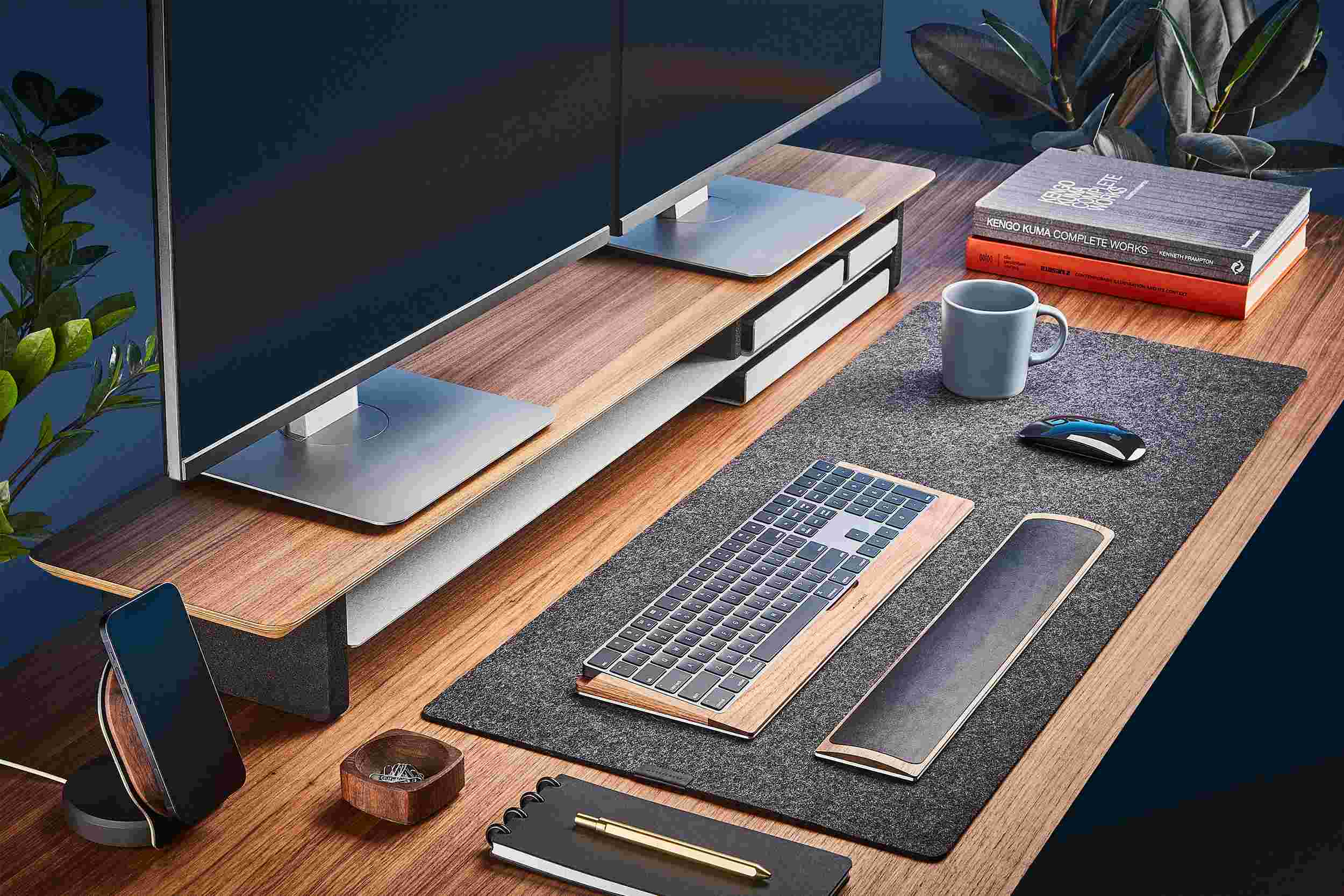 The Medium Plus Wool Felt Desk Pad runs the entire width of a standard desk, pictured here with walnut wood double-wide monitor stand.