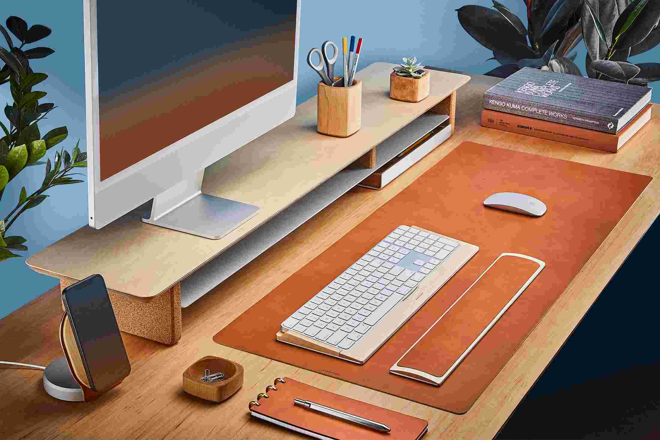 The Medium Wool Felt Desk Pad runs the entire width of a standard desk, pictured here with maple wood double-wide monitor stand.