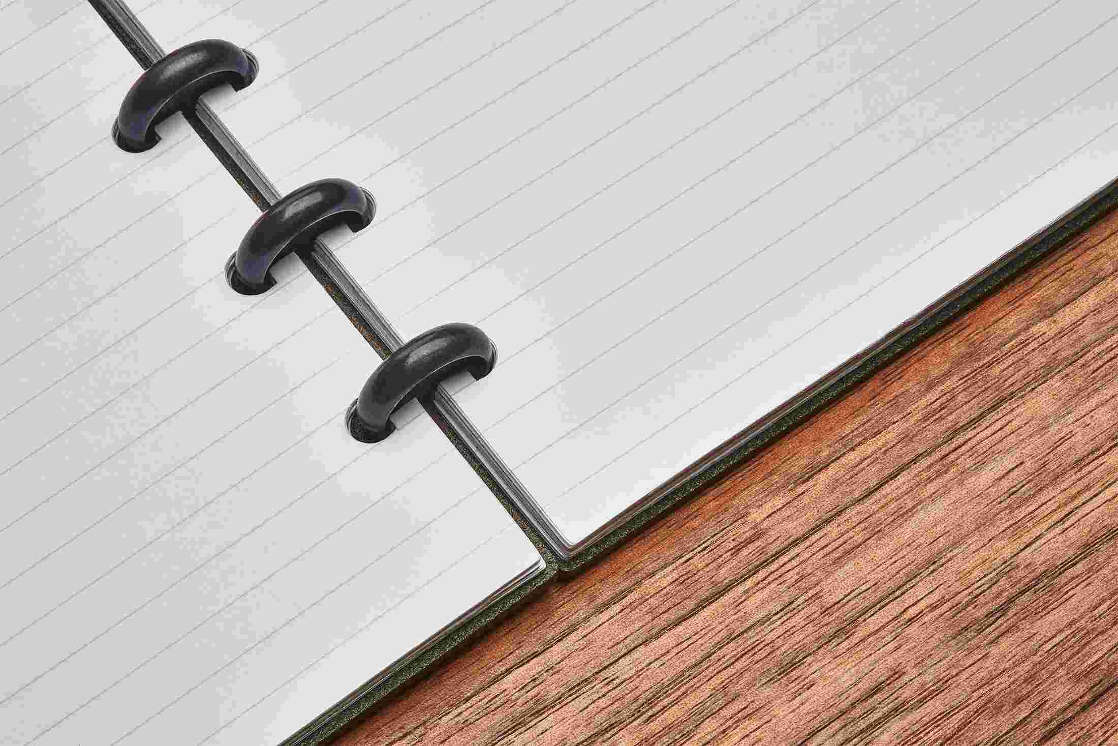 Close up detail showing the ruled notebook lying completely flat on walnut desktop.