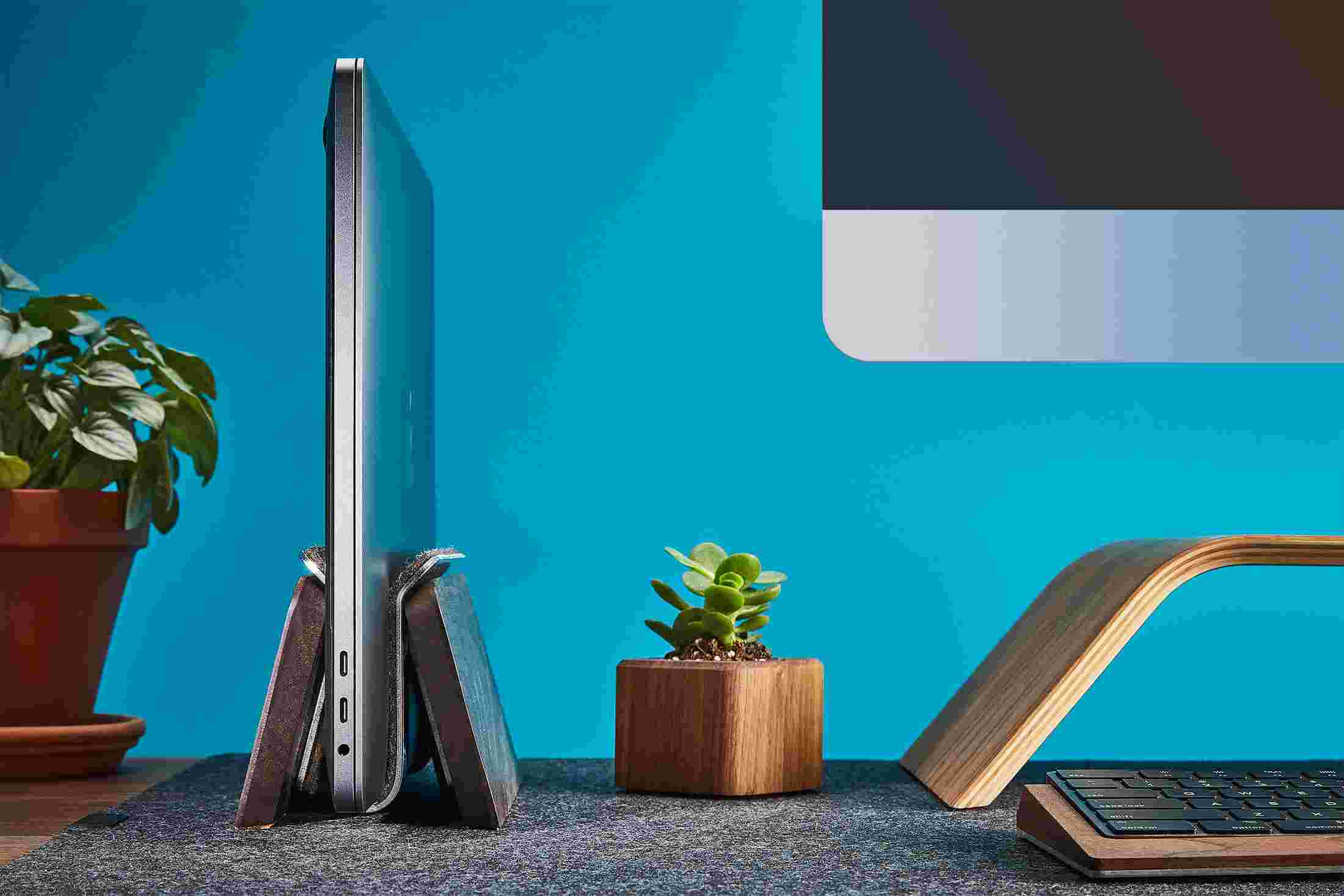 Profile view of the Walnut Vertical MacBook Stand on wool felt desk pad.