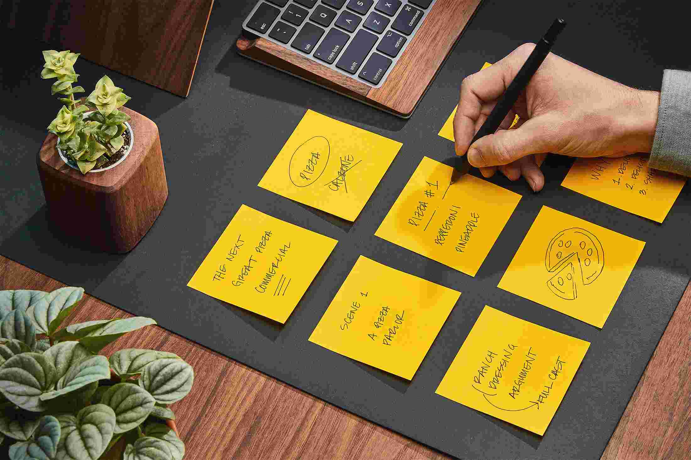 Hand writing directly on the matte black desk pad on yellow sticky notes.