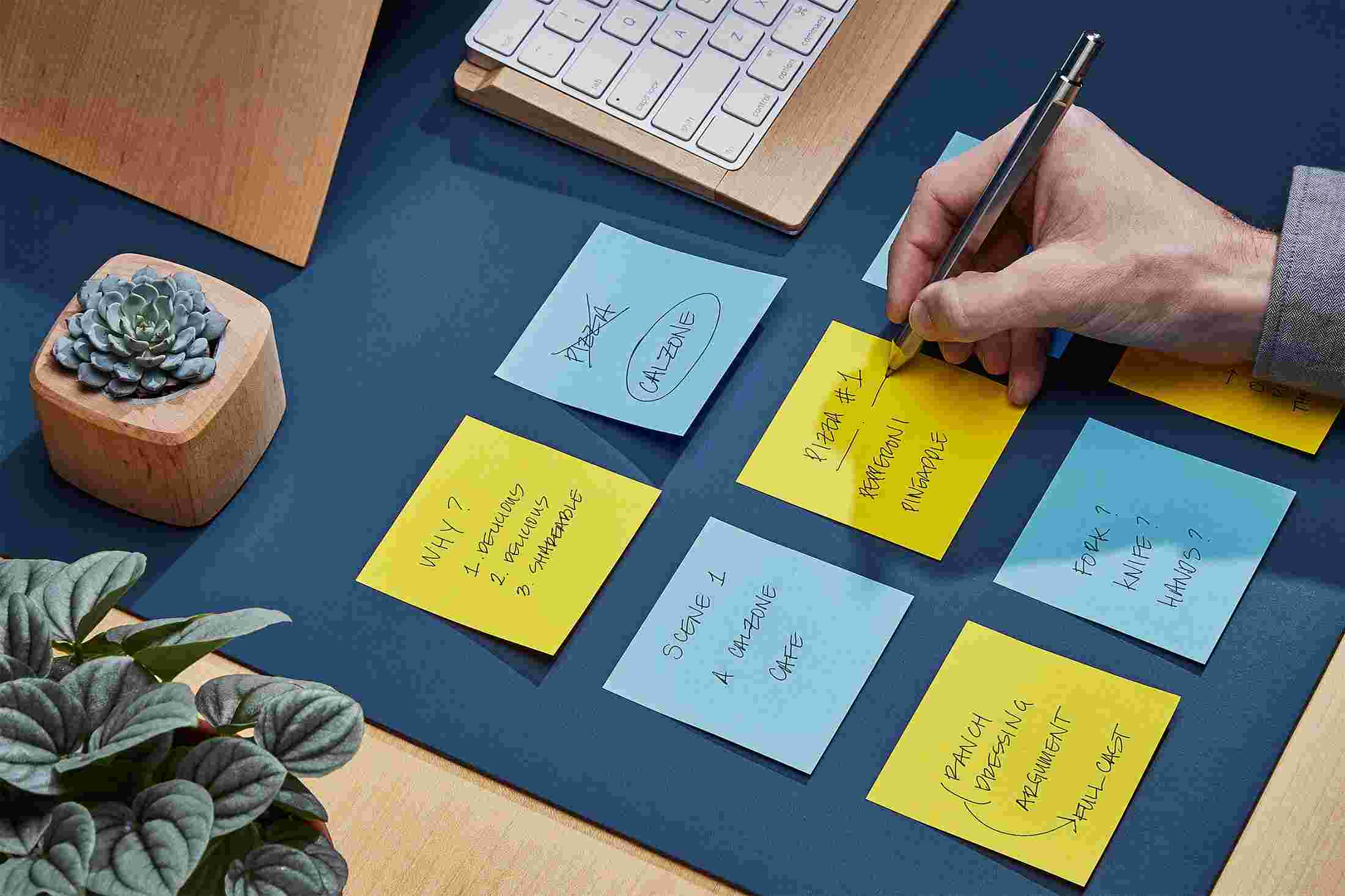 Hand writing directly on the matte blue desk pad on sticky notes.