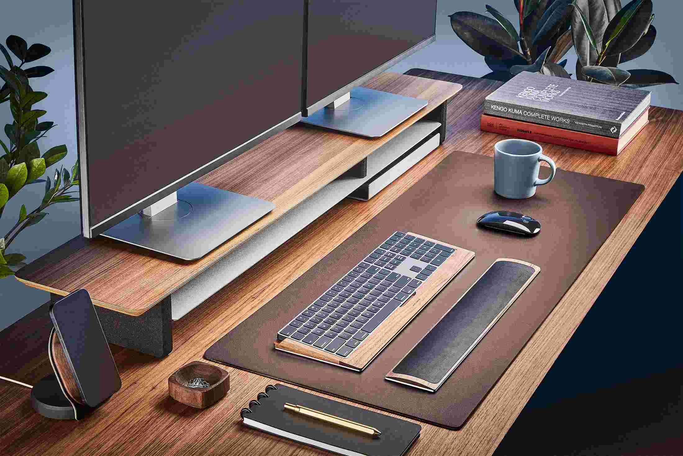 The Medium Matte Desk Pad in Brown runs the entire width of a standard desk, pictured here with walnut wood double-wide monitor stand.