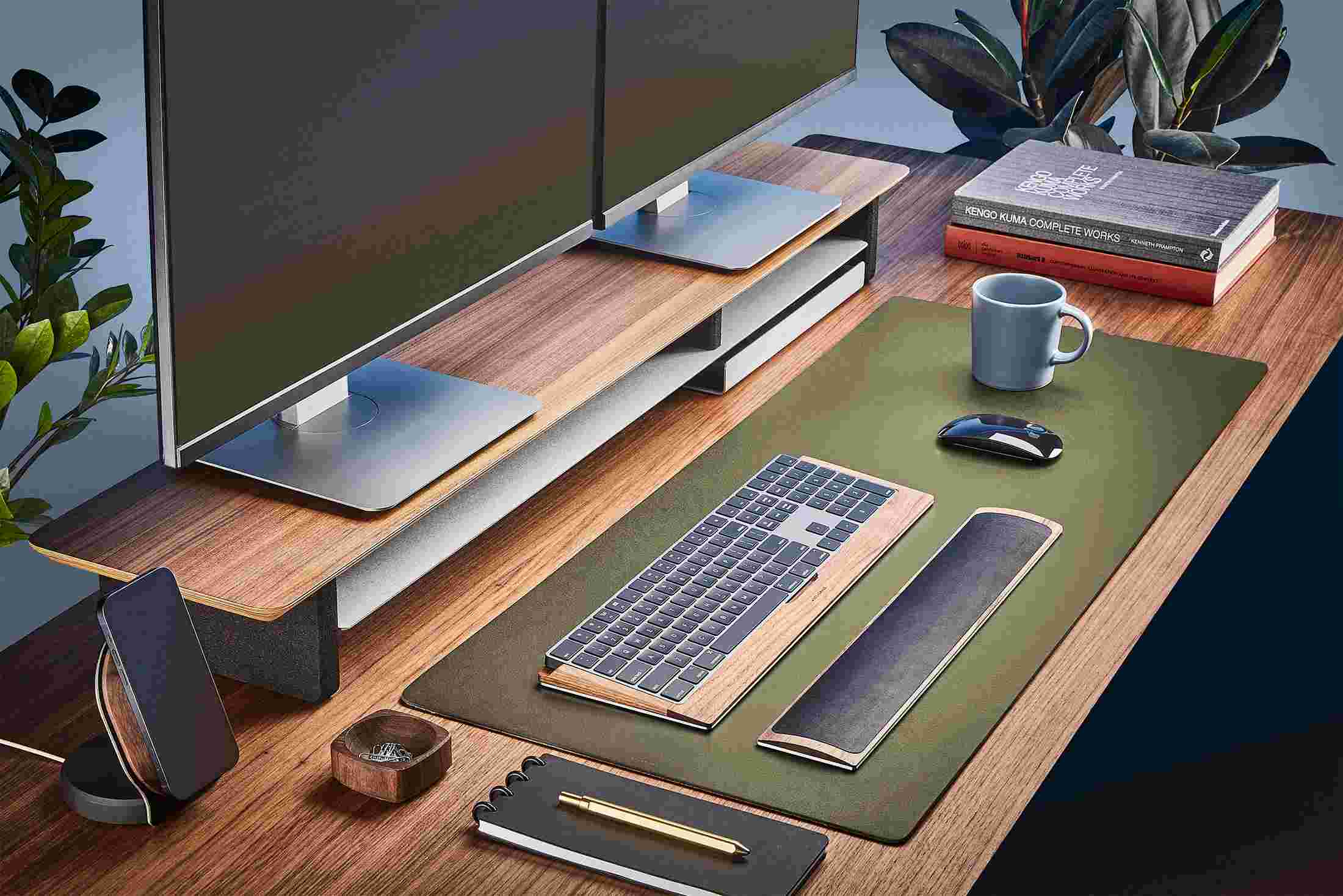 The Medium Matte Desk Pad in Dark Green runs the entire width of a standard desk, pictured here with walnut wood double-wide monitor stand.