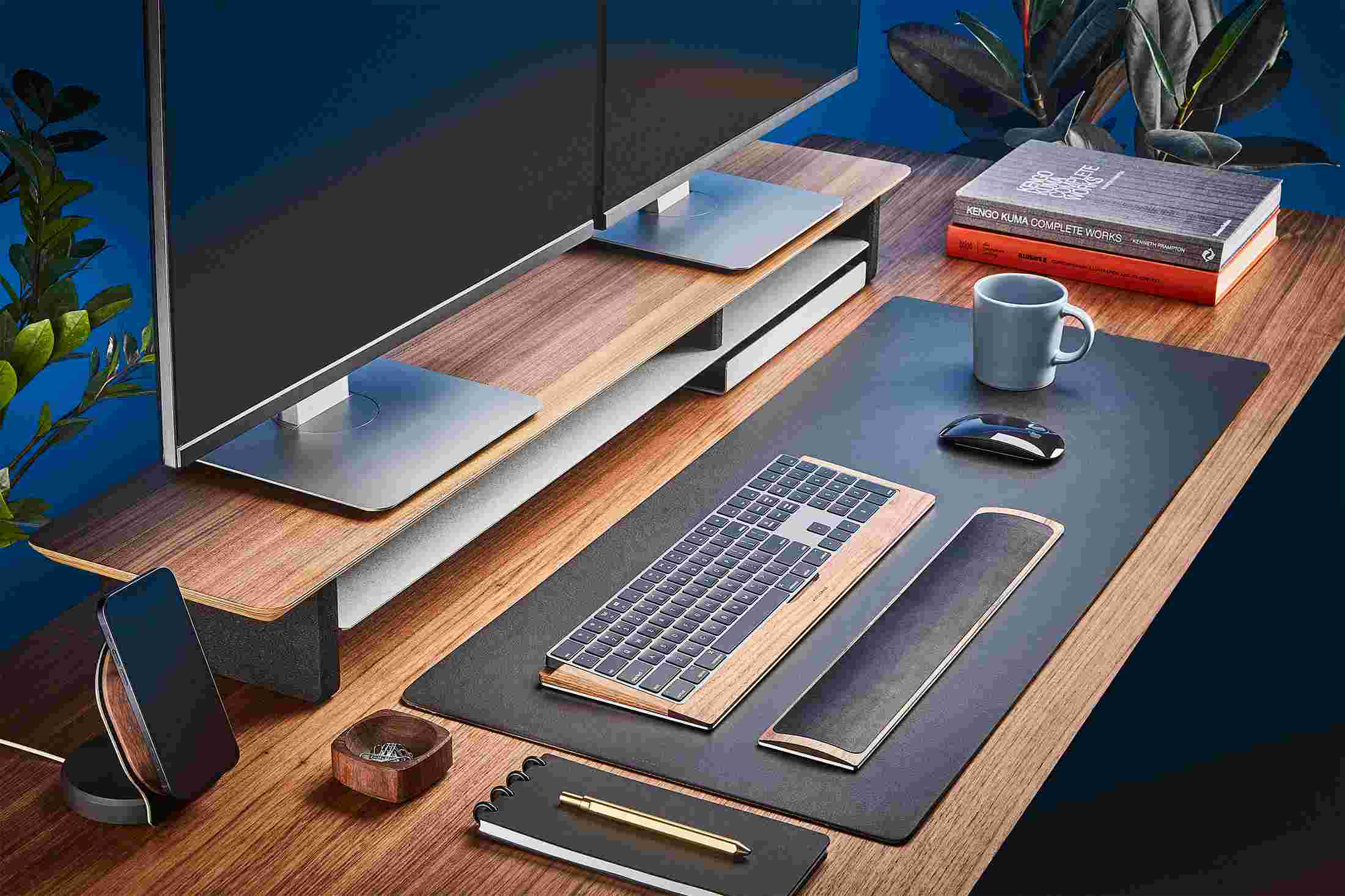 The Medium Matte Black Desk Pad runs the entire width of a standard desk, pictured here with walnut wood double-wide monitor stand.