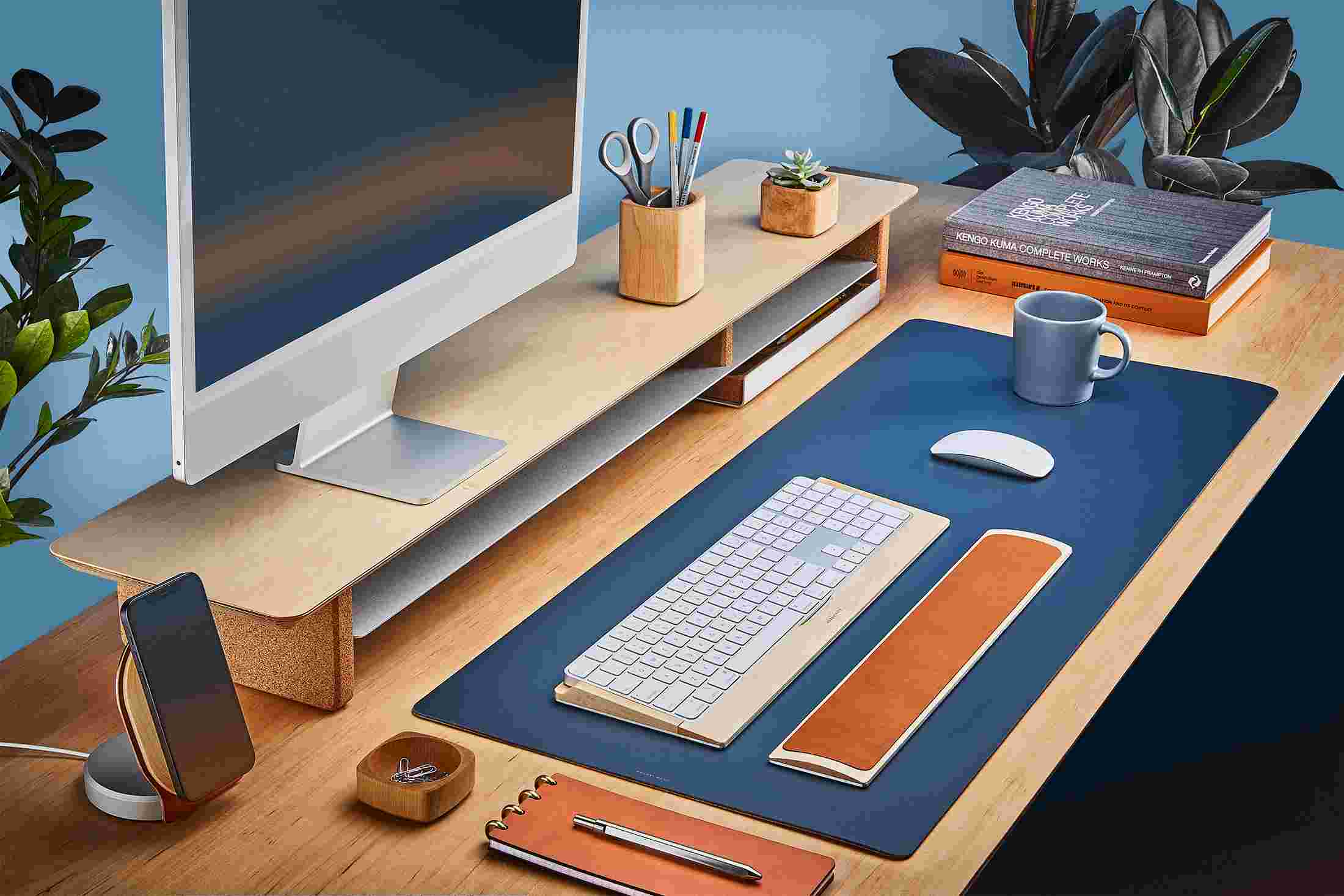 The Medium Matte Desk Pad in Navy Blue runs the entire width of a standard desk, pictured here with maple wood double-wide monitor stand.
