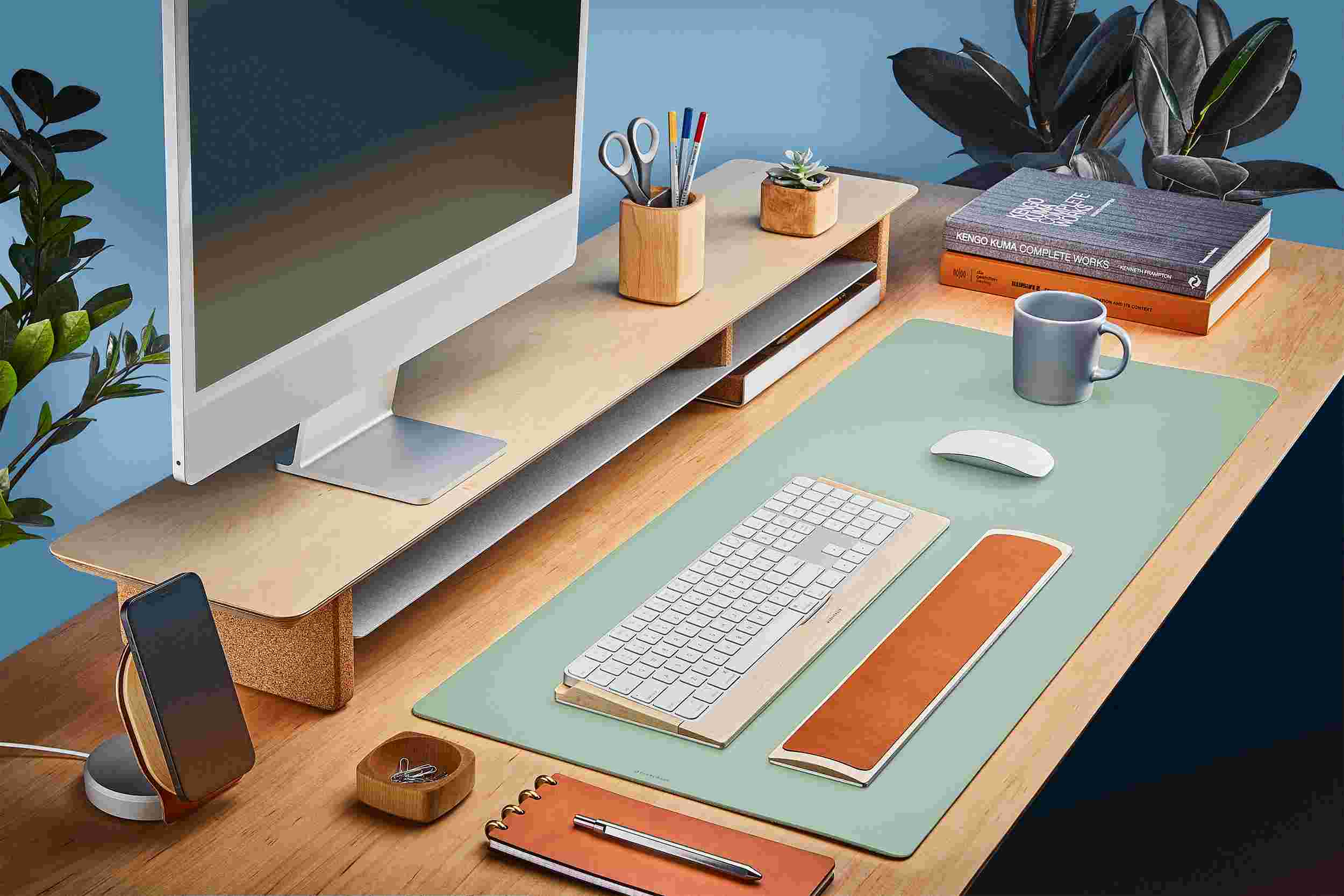The Medium Matte Desk Pad in Light Green runs the entire width of a standard desk, pictured here with maple wood double-wide monitor stand.