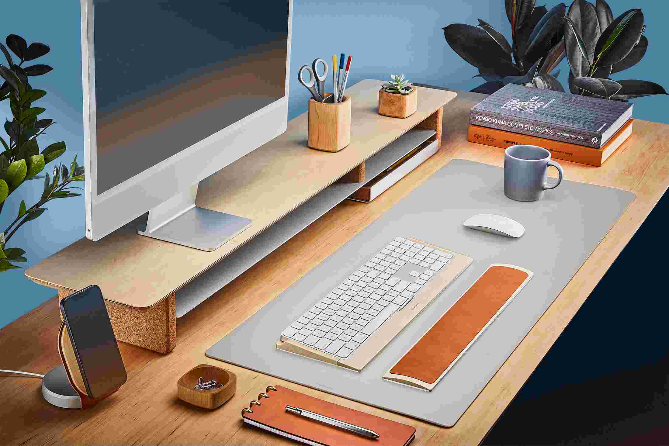 The Medium Matte Desk Pad in Light Grey runs the entire width of a standard desk, pictured here with maple wood double-wide monitor stand.