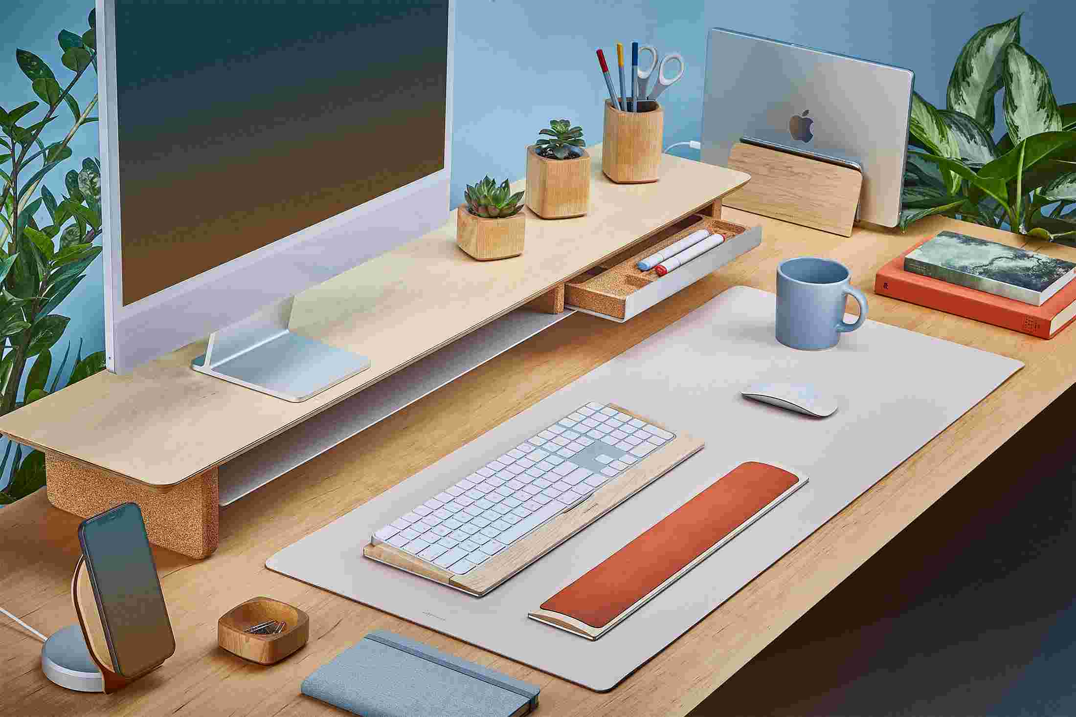 The Medium Plus Matte Desk Pad in Pink runs the entire width of a standard desk, pictured here with maple wood double-wide monitor stand.