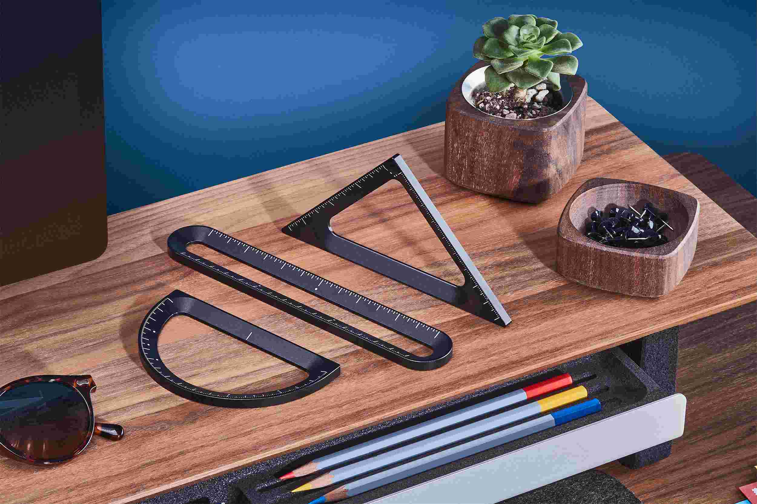 Set of three Grovemade measuring tools—ruler, triangle, and protractor—displayed on a walnut desk shelf.