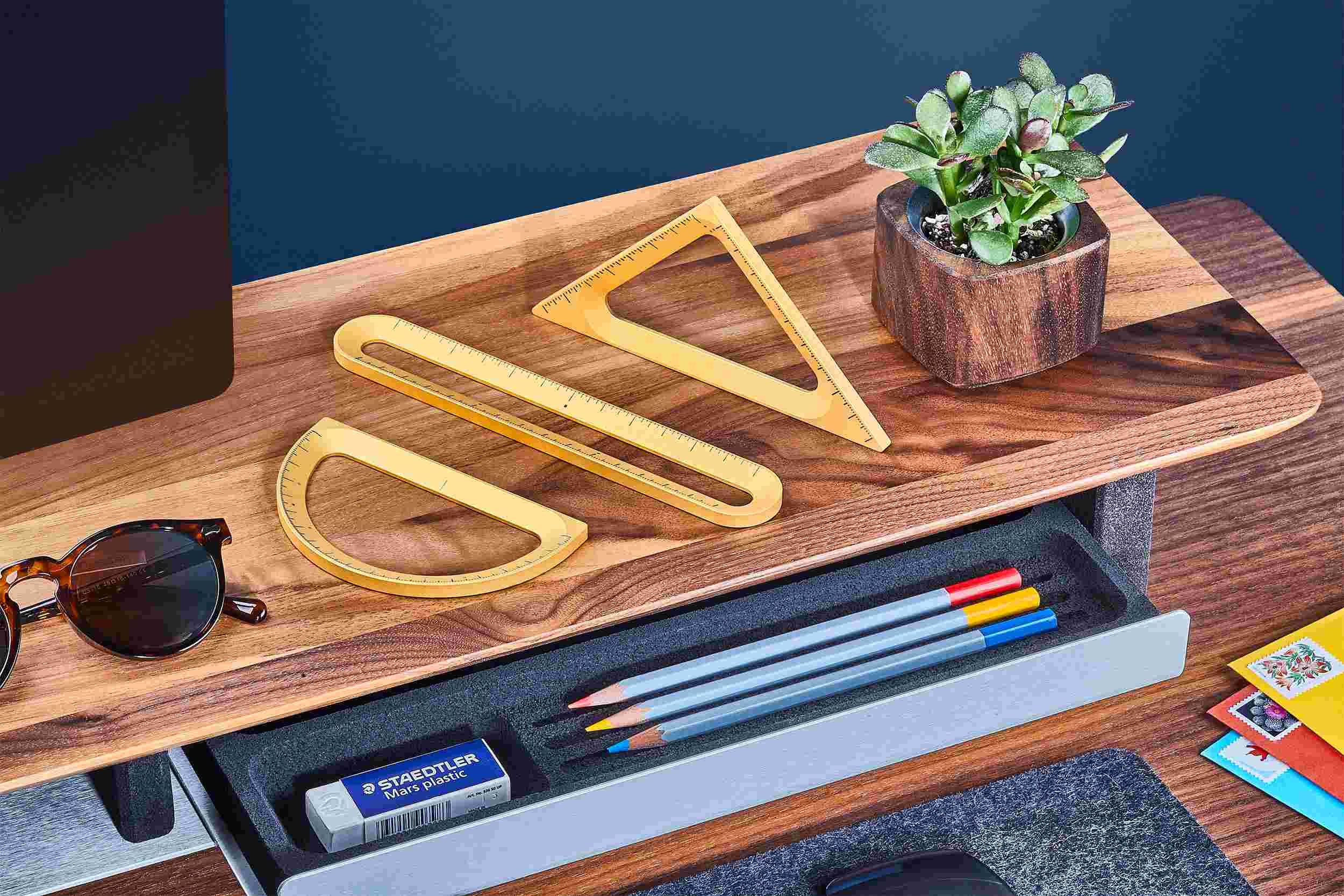 Set of three gold Grovemade measuring tools—ruler, triangle, and protractor—displayed on a walnut desk shelf.