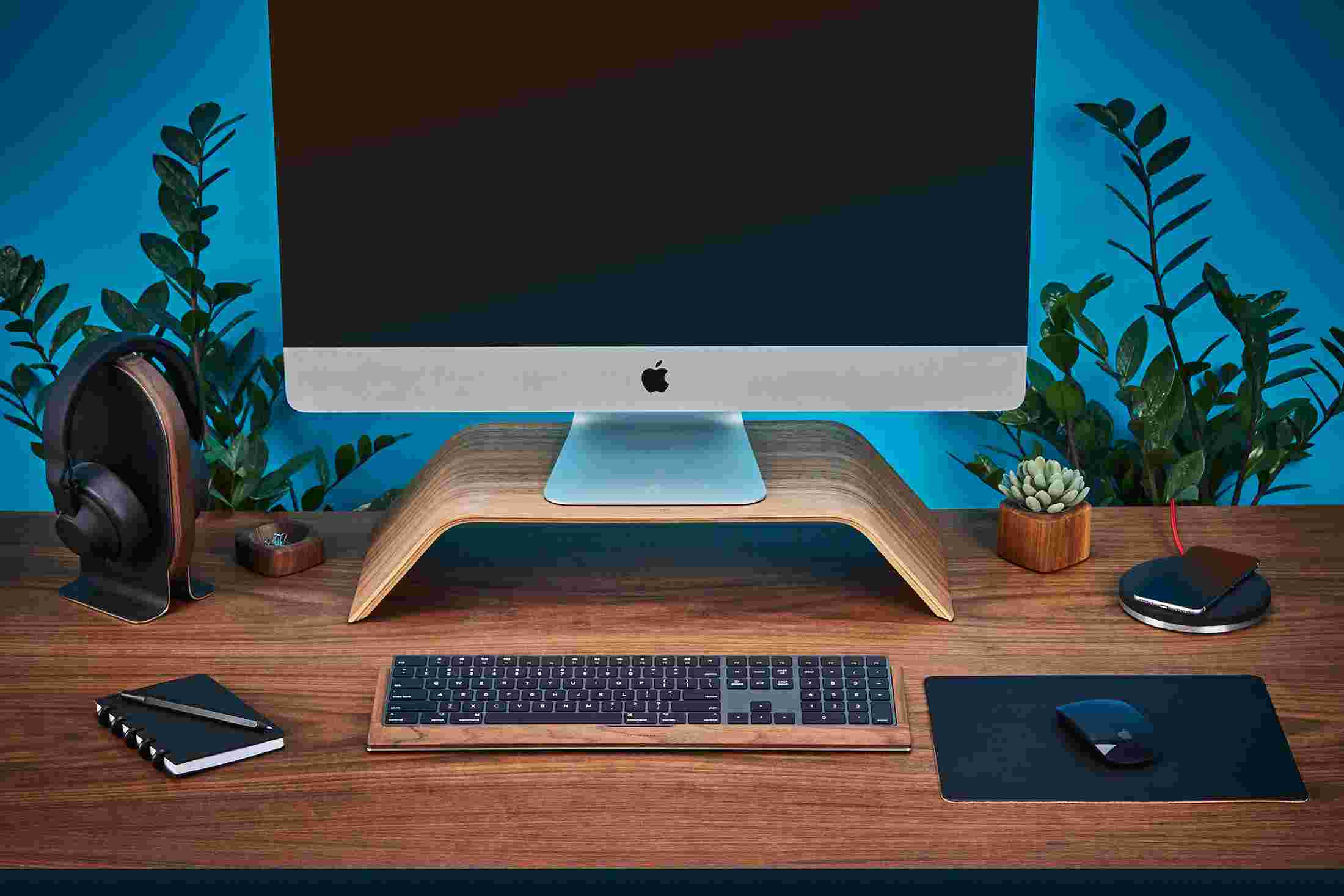 Wood monitor stand on walnut desktop with large black leather mouse pad.