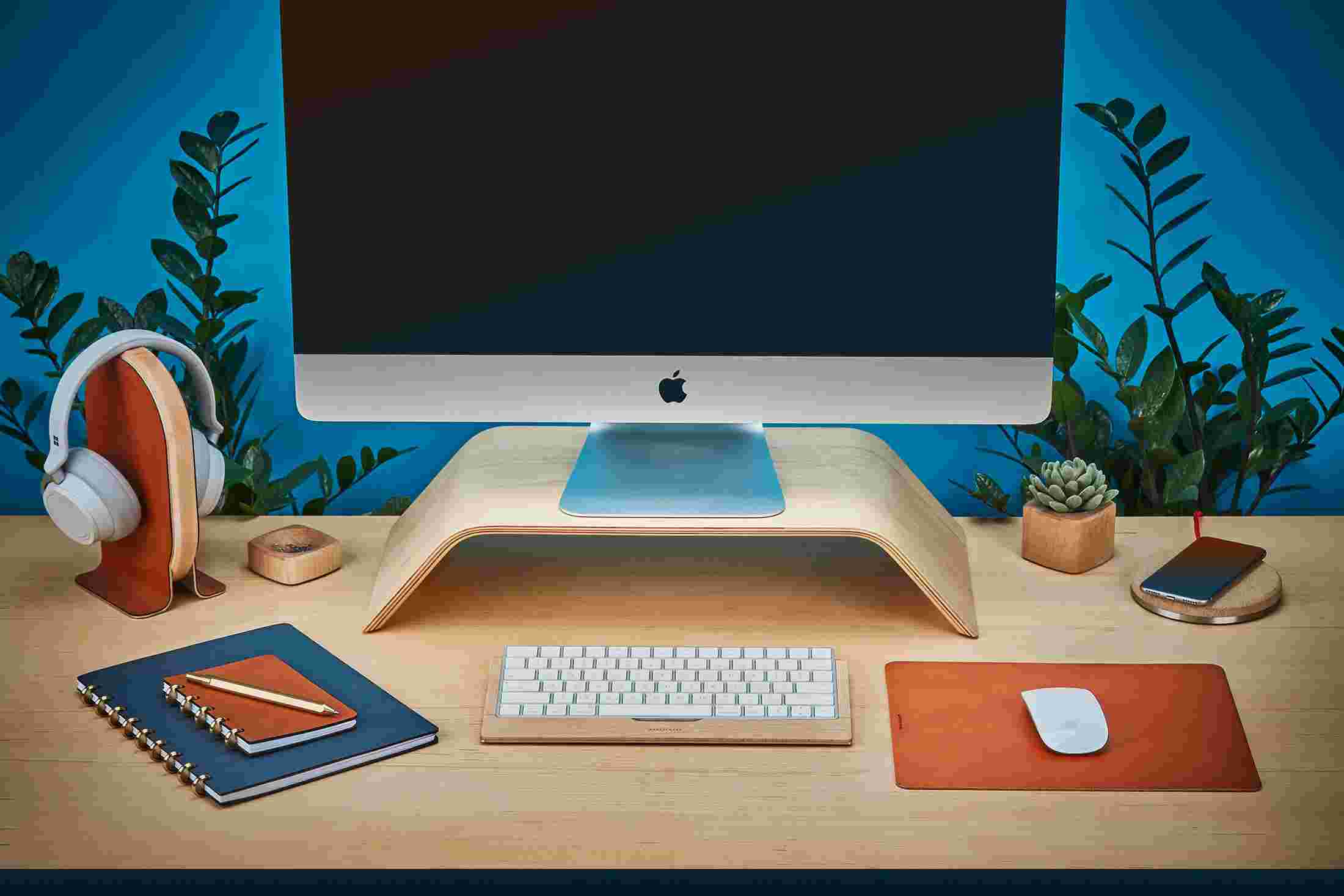 Wood monitor stand on maple desktop with large tan leather mouse pad.