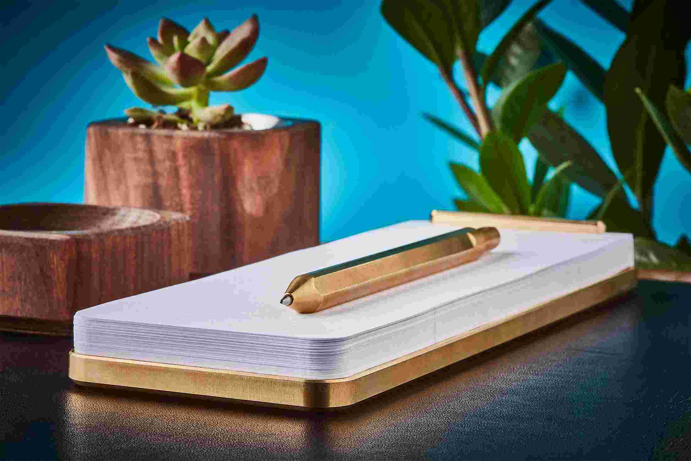 Profile view of tan metal desk notepad on black leather desk pad.