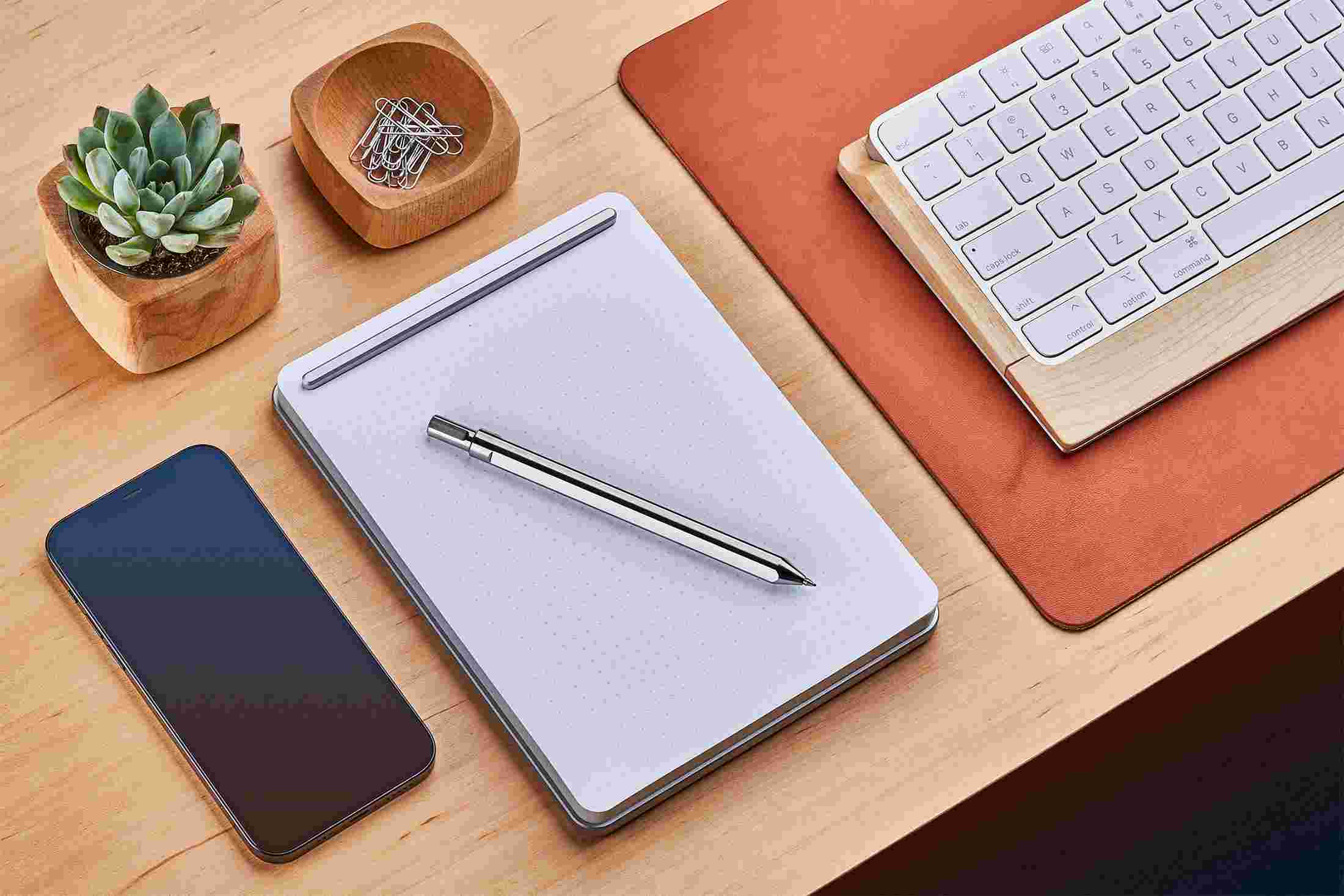Large silver notepad on maple desk next to tan leather desk pad.
