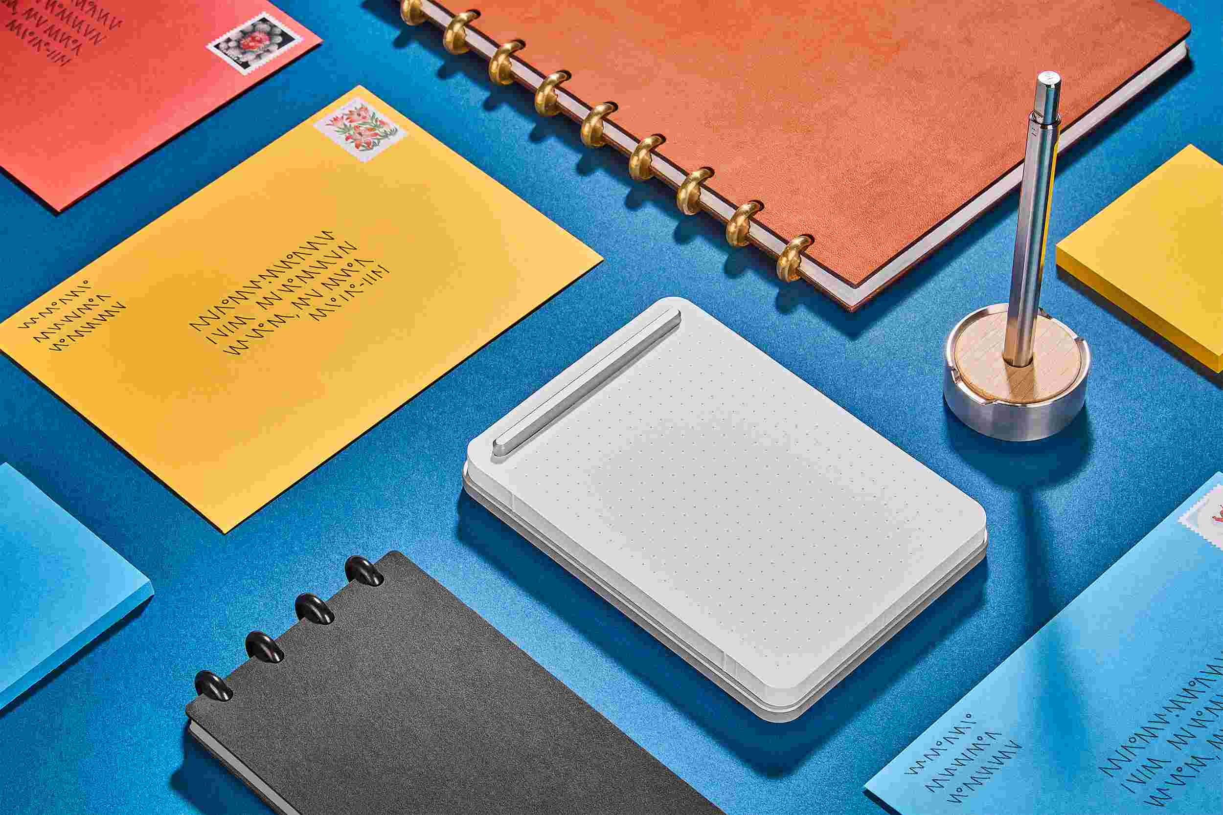 Silver notepad with matching titanium pen and maple stand on bright blue background.