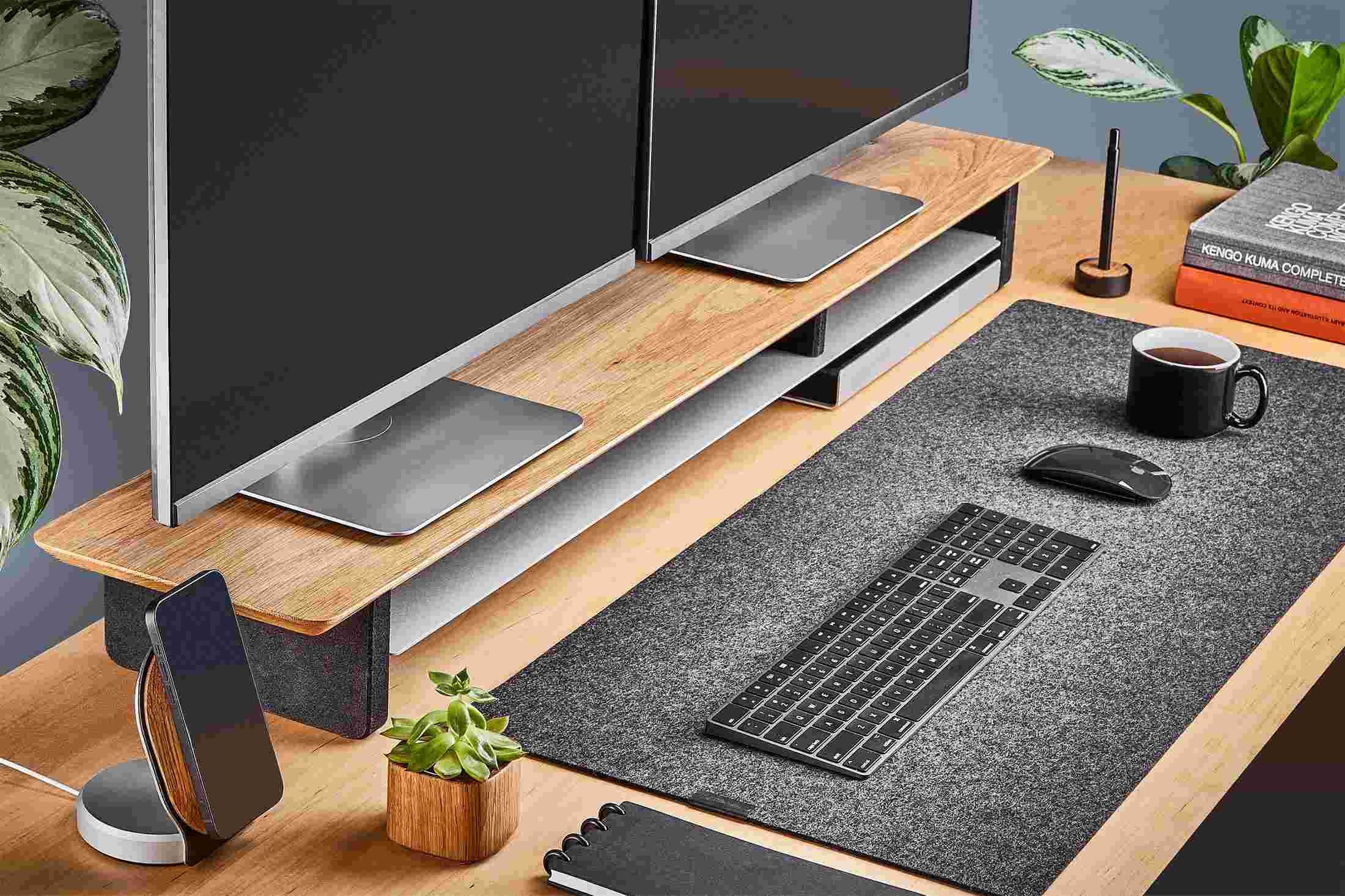 The Medium Wool Felt Desk Pad runs the entire width of a standard desk, pictured here with solid white oak double-wide monitor stand.