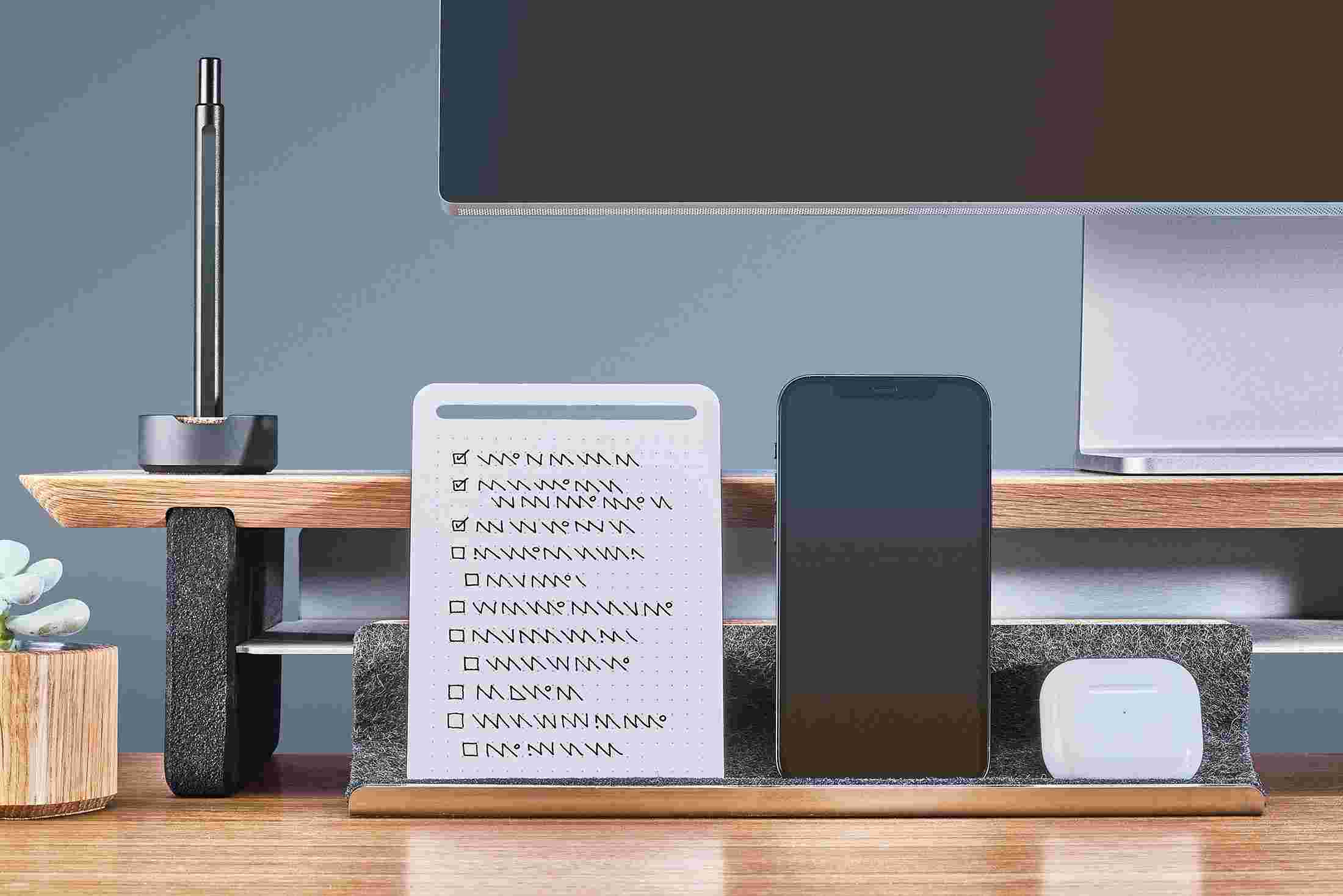 The Oak Display Rail propping up an iPhone and notes, and acting as a home for an AirPods case.