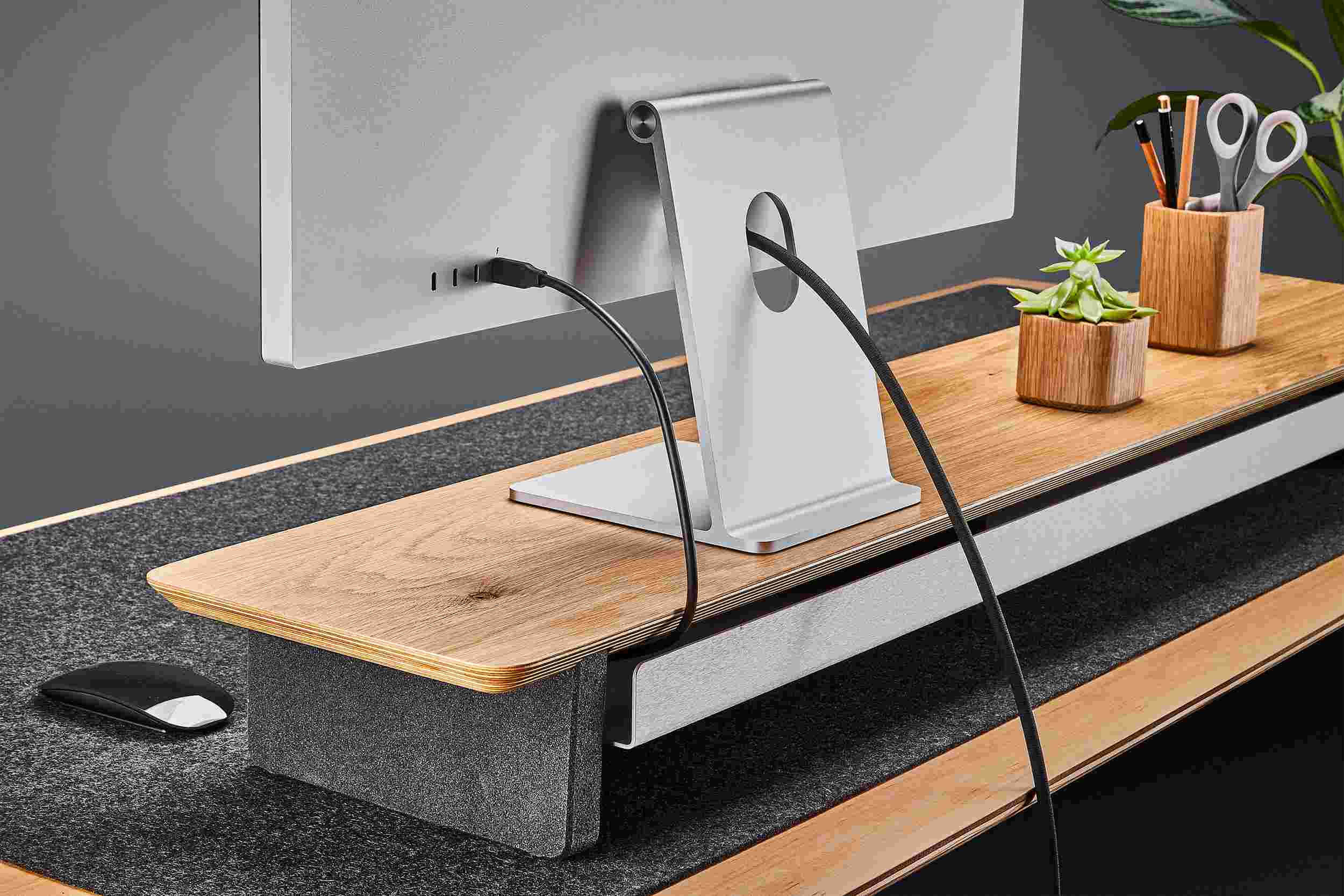 Ultra-wide oak plywood desk shelf for double monitor setup, with dark merino wool felt desk pad.