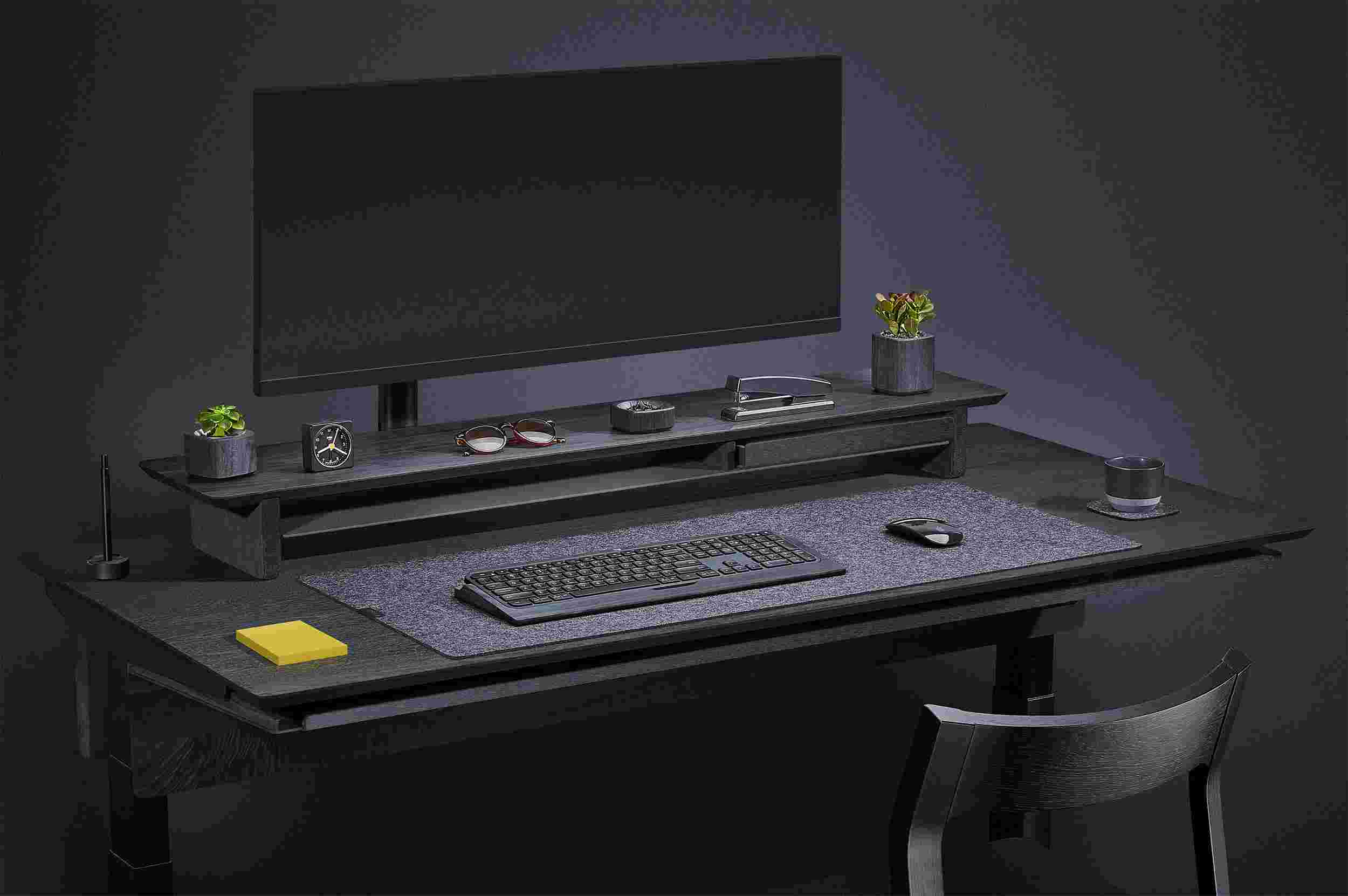 Side view of the blackened walnut standing desk with monitor arm and premium felt desk pad.
