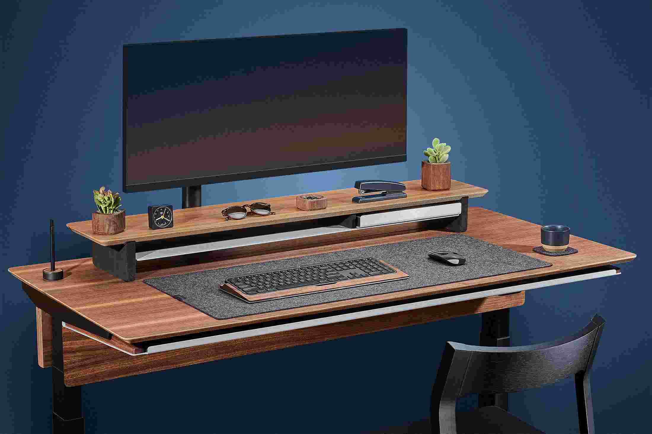 Side view of the walnut plywood standing desk with monitor arm and premium felt desk pad.