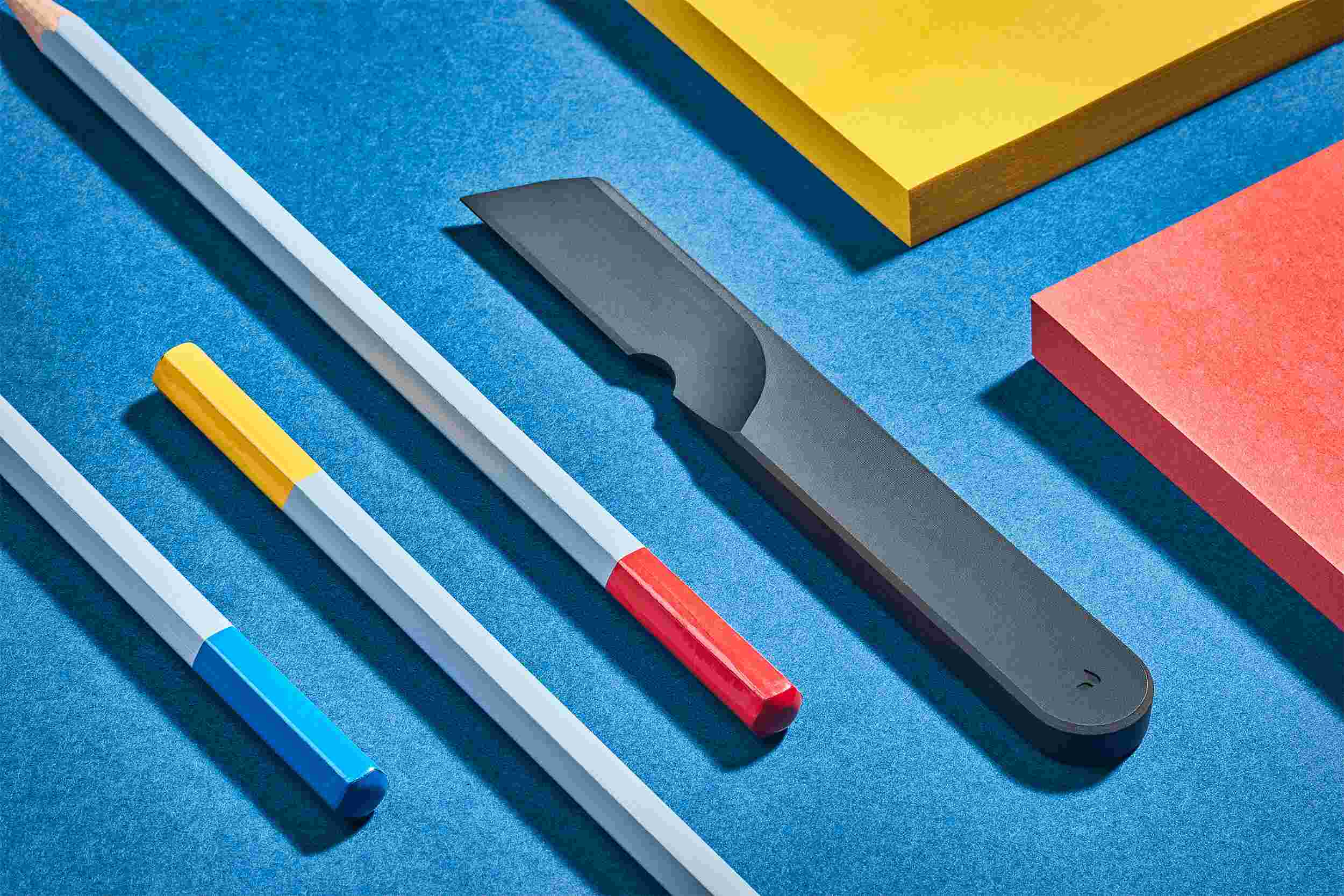 Sculptural matte black task knife on blue background.