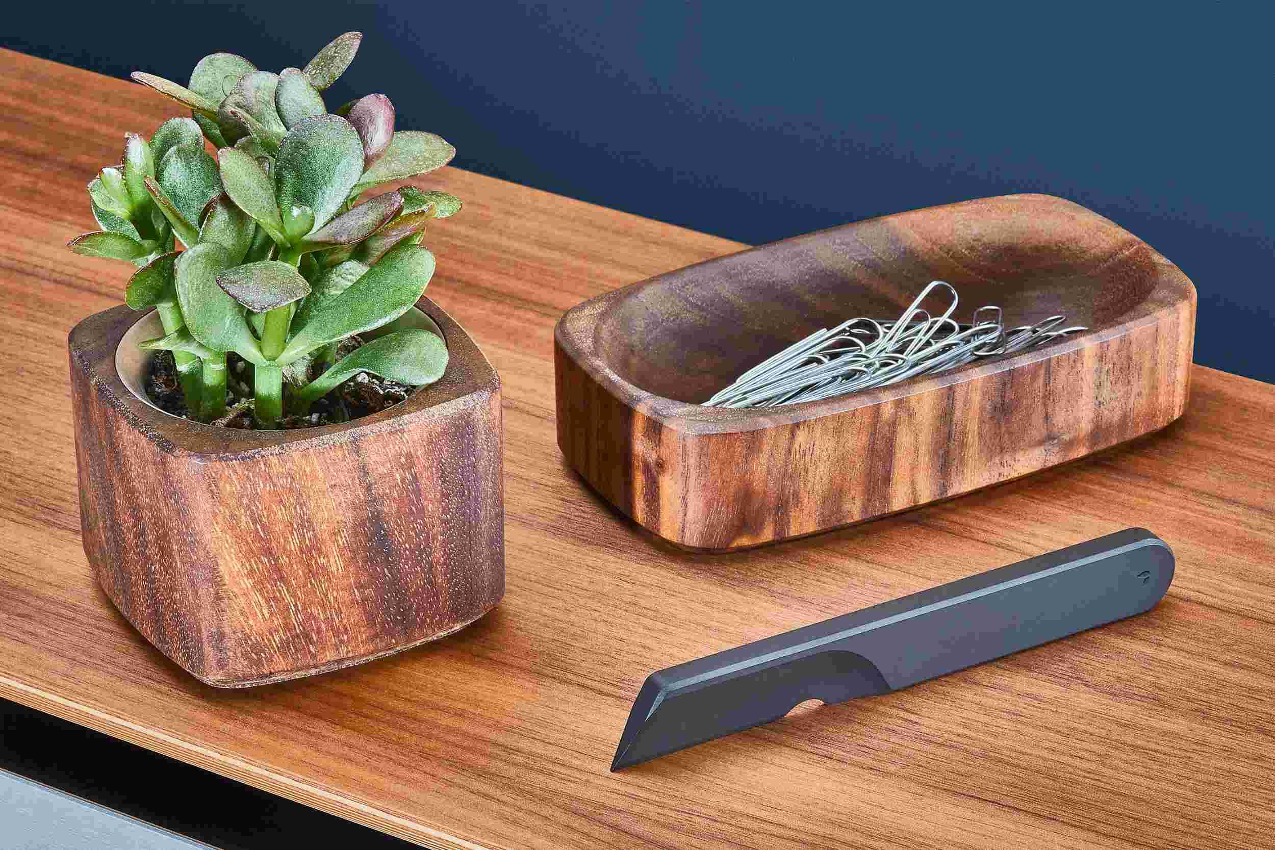 Matte black task knife on walnut desk shelf with matching planter and dish.