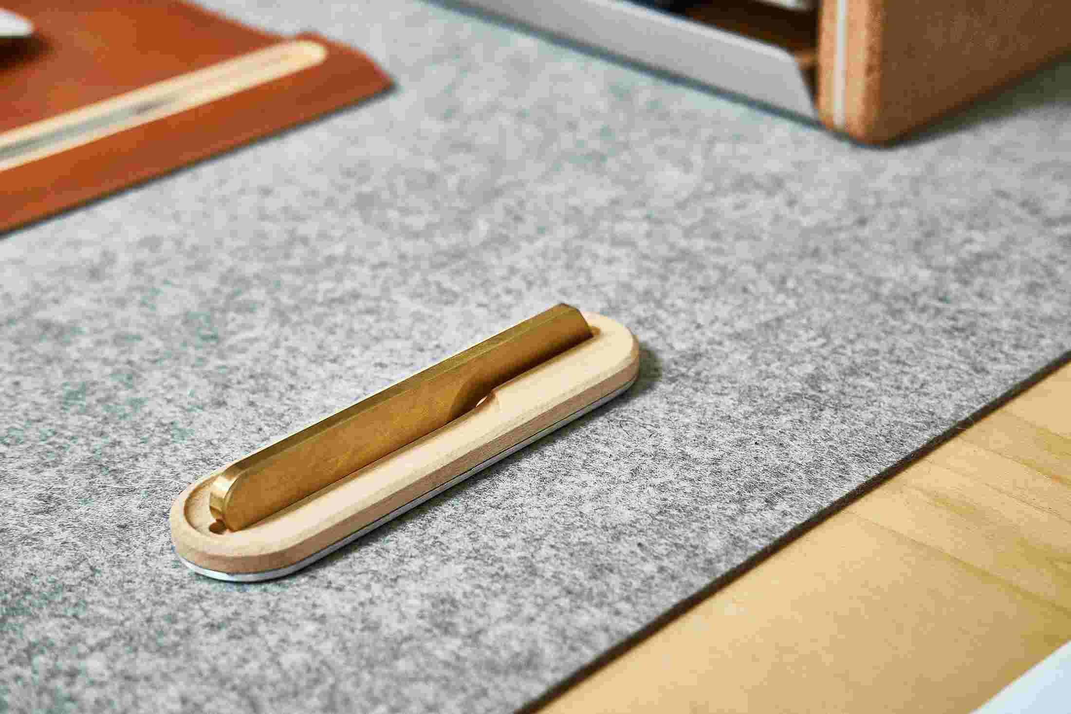 Brass one piece knife with maple stand on wool felt desk pad.