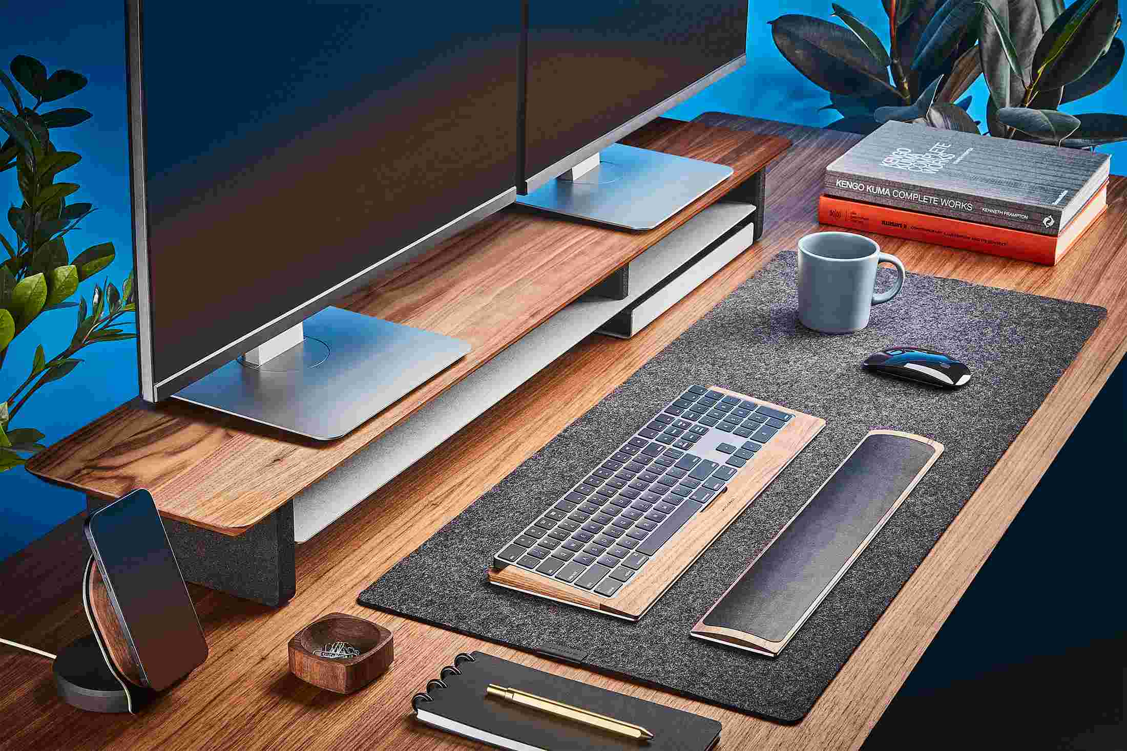 The Medium Wool Felt Desk Pad runs the entire width of a standard desk, pictured here with solid walnut wood double-wide monitor stand.