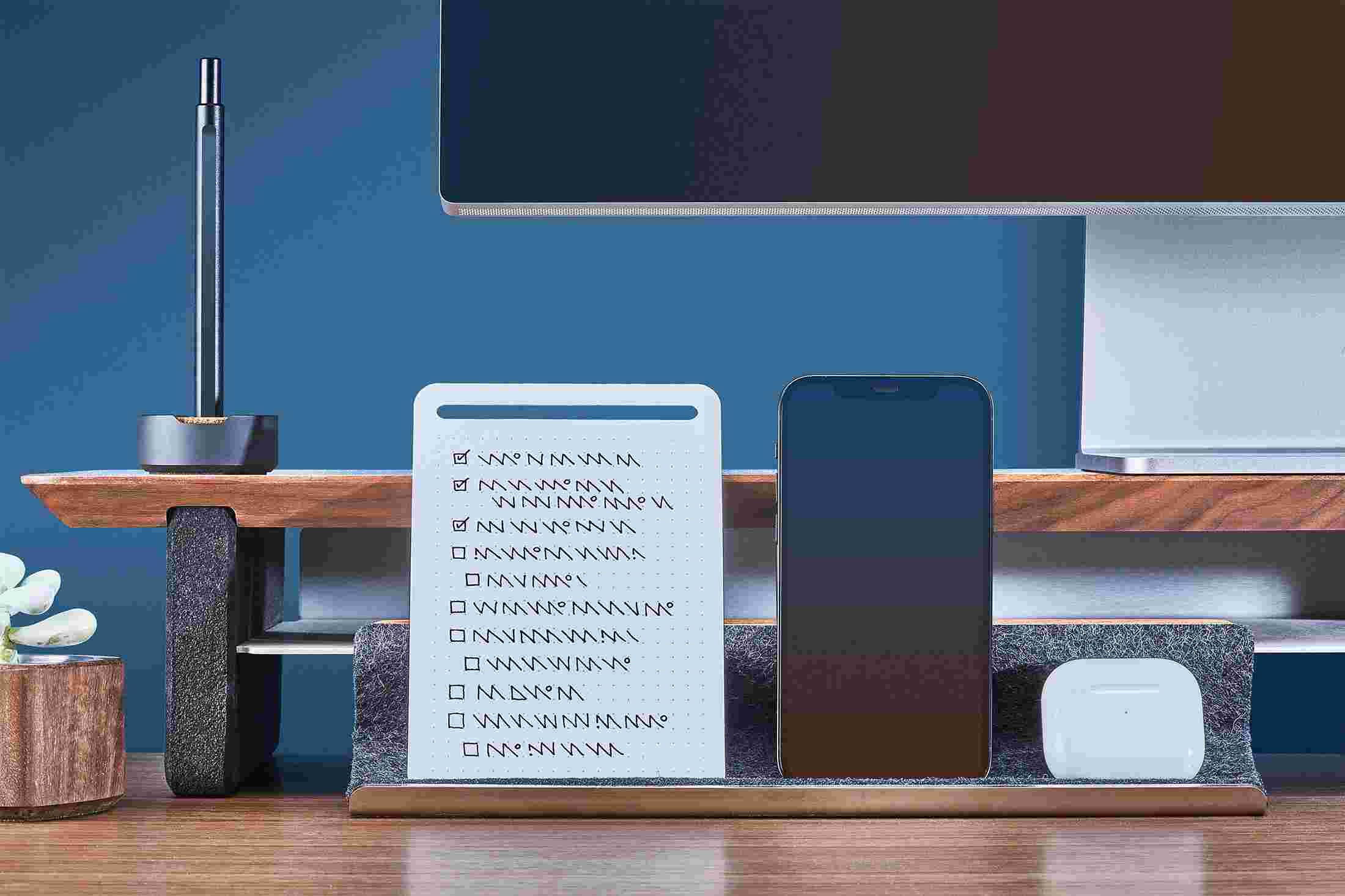 The Walnut Display Rail propping up an iPhone and notes, and acting as a home for an AirPods case.
