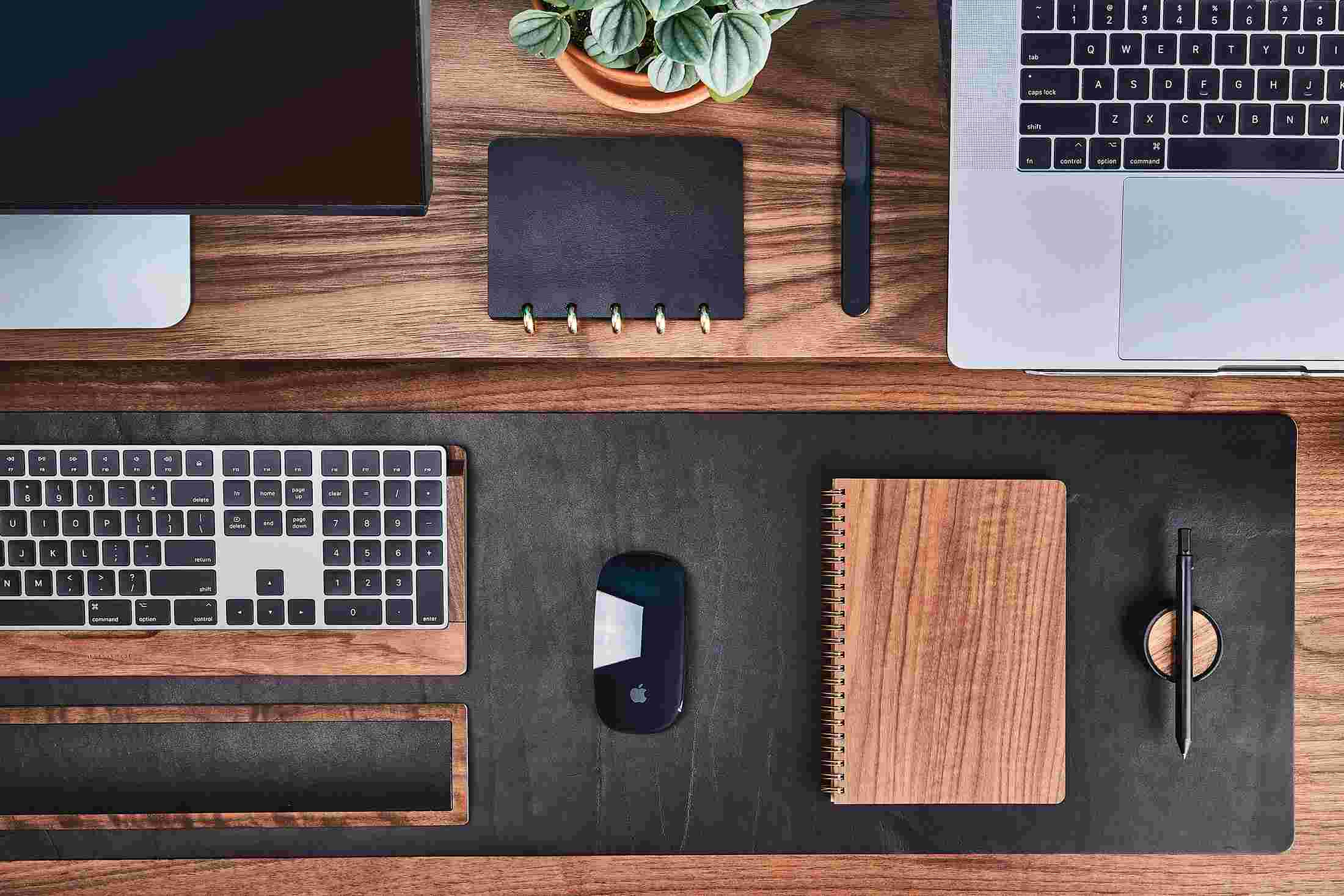 Overhead of walnut and leather notebooks on black leather desk pad with wooden keyboard tray.